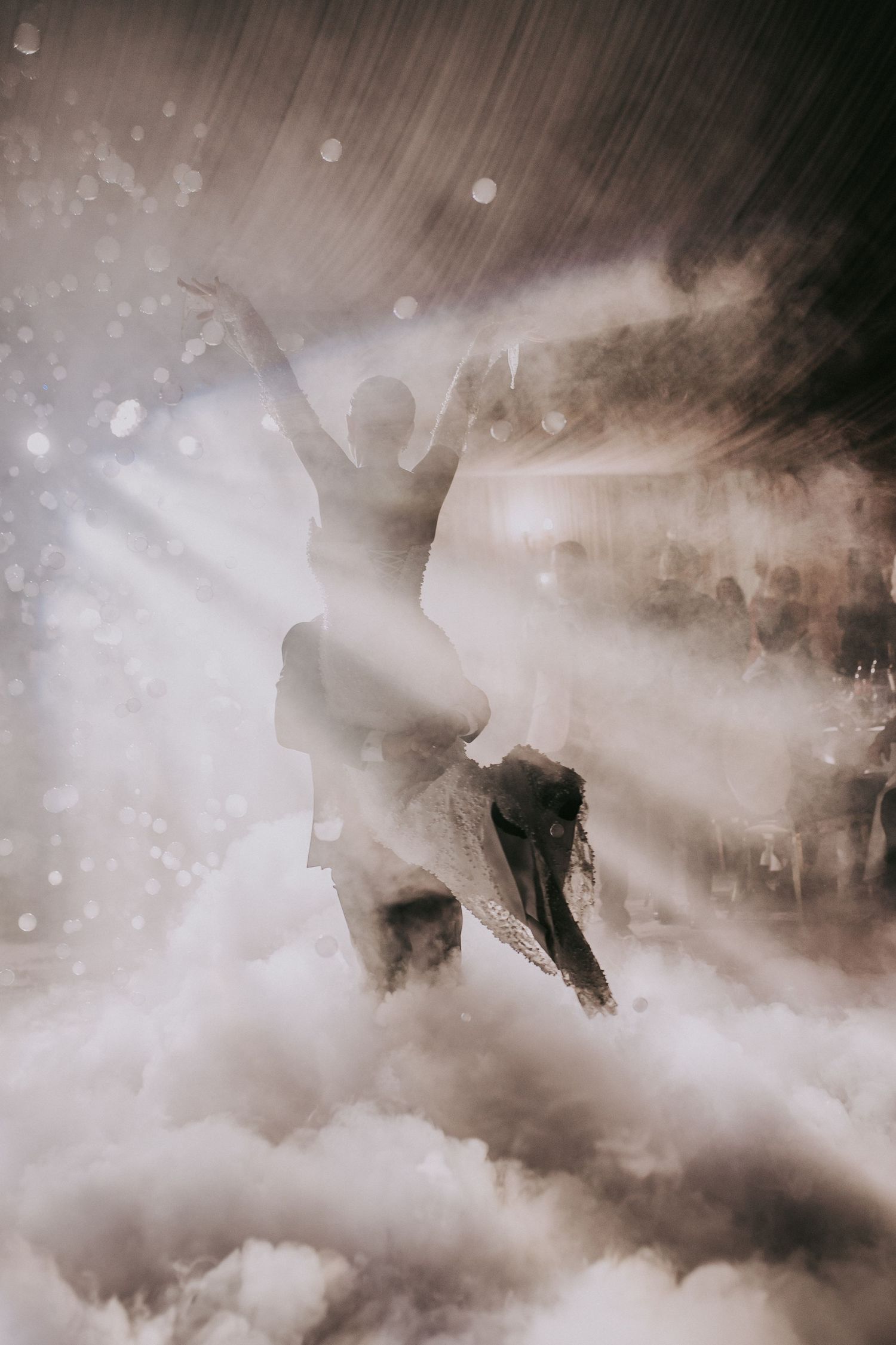 Dreamy artistic shot of couple dancing in swirling fog and light rays at their wedding celebration.