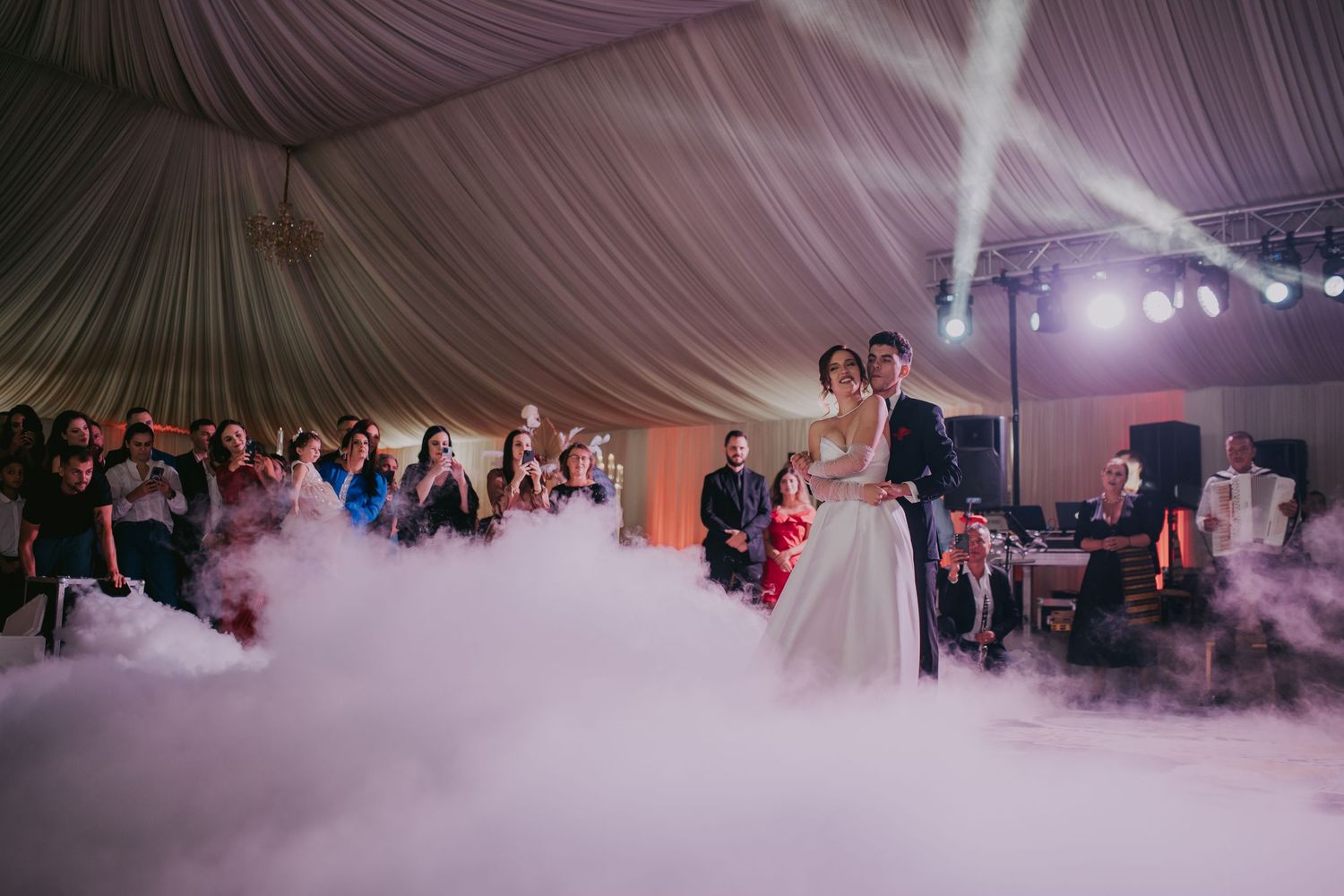 Bride and groom share first dance on fog-covered dance floor inside elegant white tent venue. Epicu Fotograf Drobeta-Turnu Severin