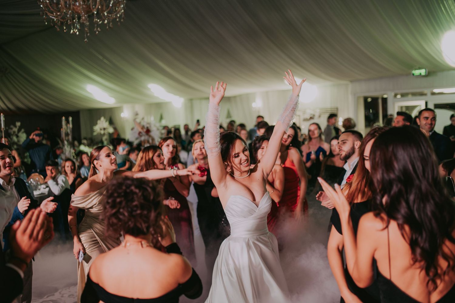 Joyful bride raises arms on crowded wedding dance floor surrounded by celebrating guests. Epicu Fotograf Drobeta-Turnu Severin