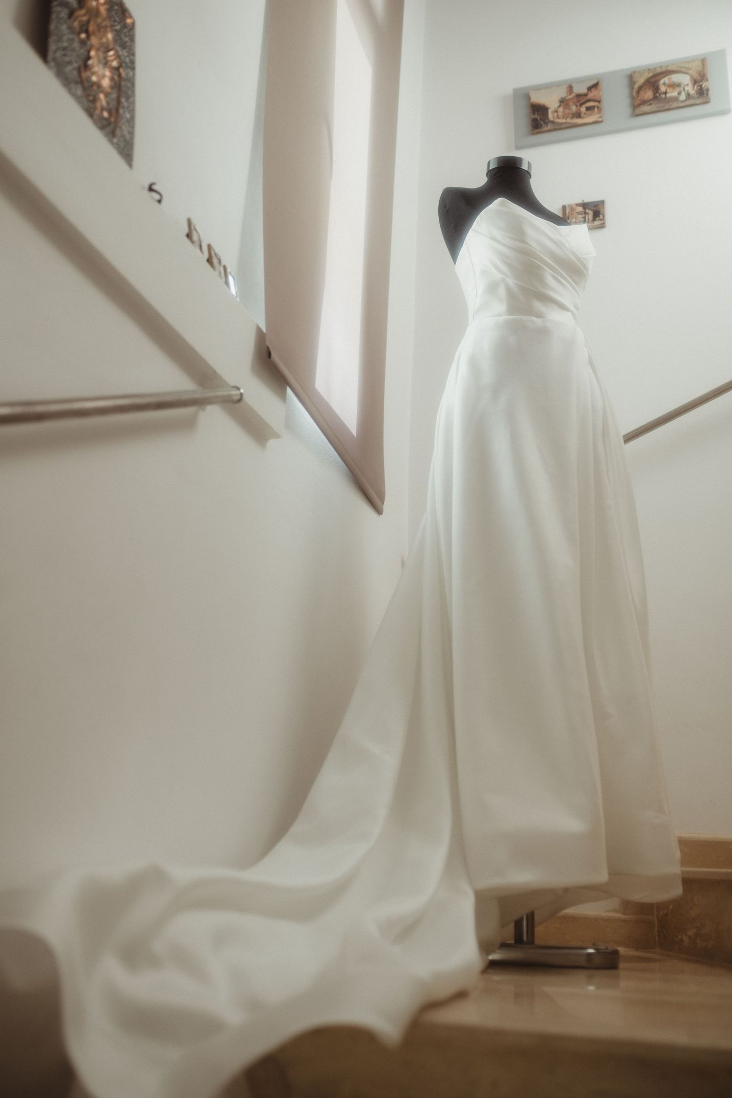 Elegant white strapless wedding gown with long train displayed on mannequin on staircase.
