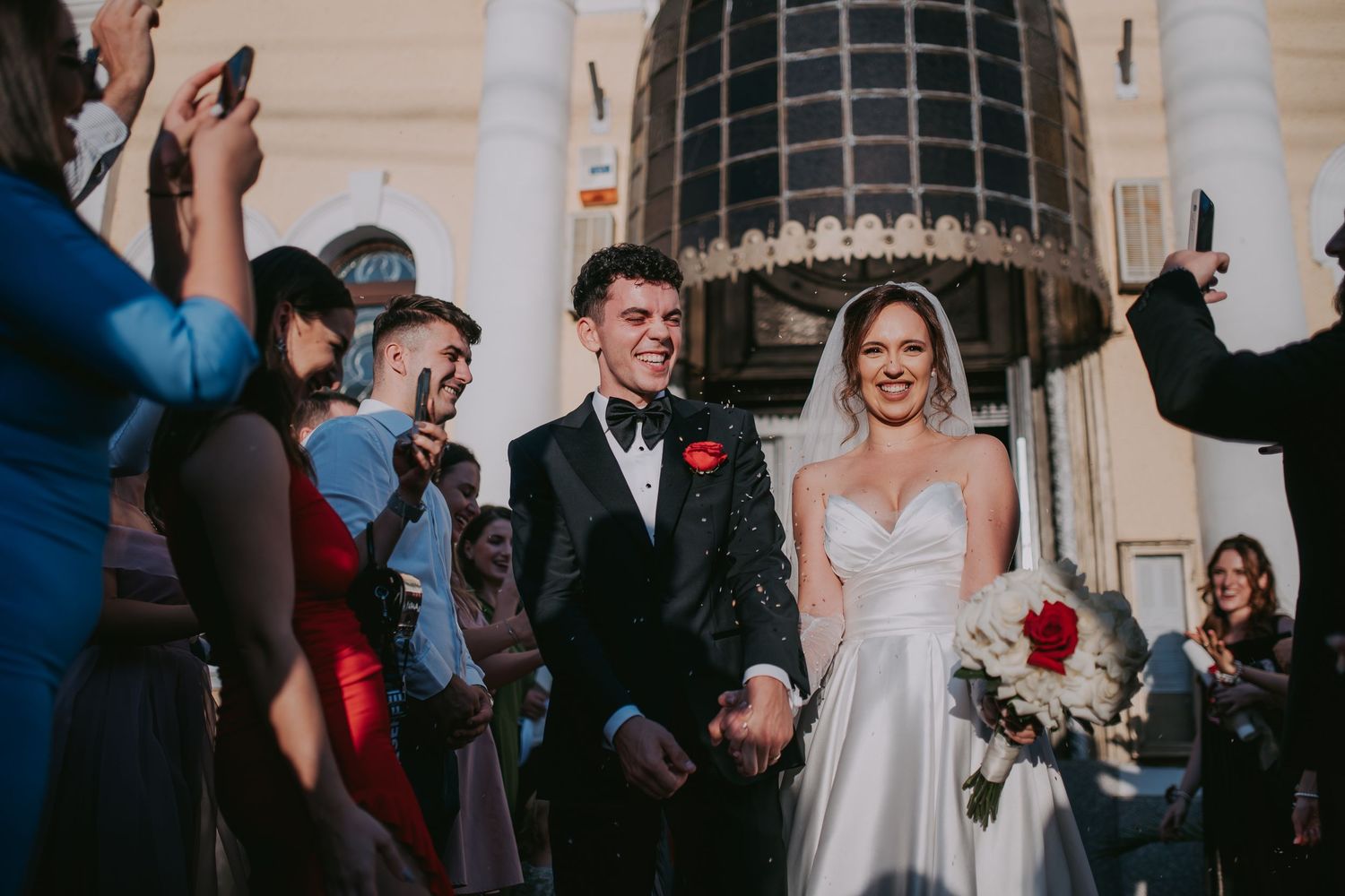 Smiling newlyweds exit Orthodox church surrounded by cheering wedding guests. Epicu Fotograf Drobeta-Turnu Severin