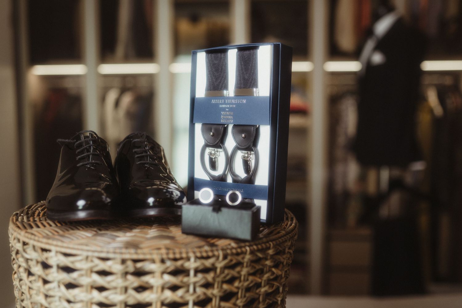 Classic brown oxford shoes beside a formal accessories set on a wicker table in a suit shop.