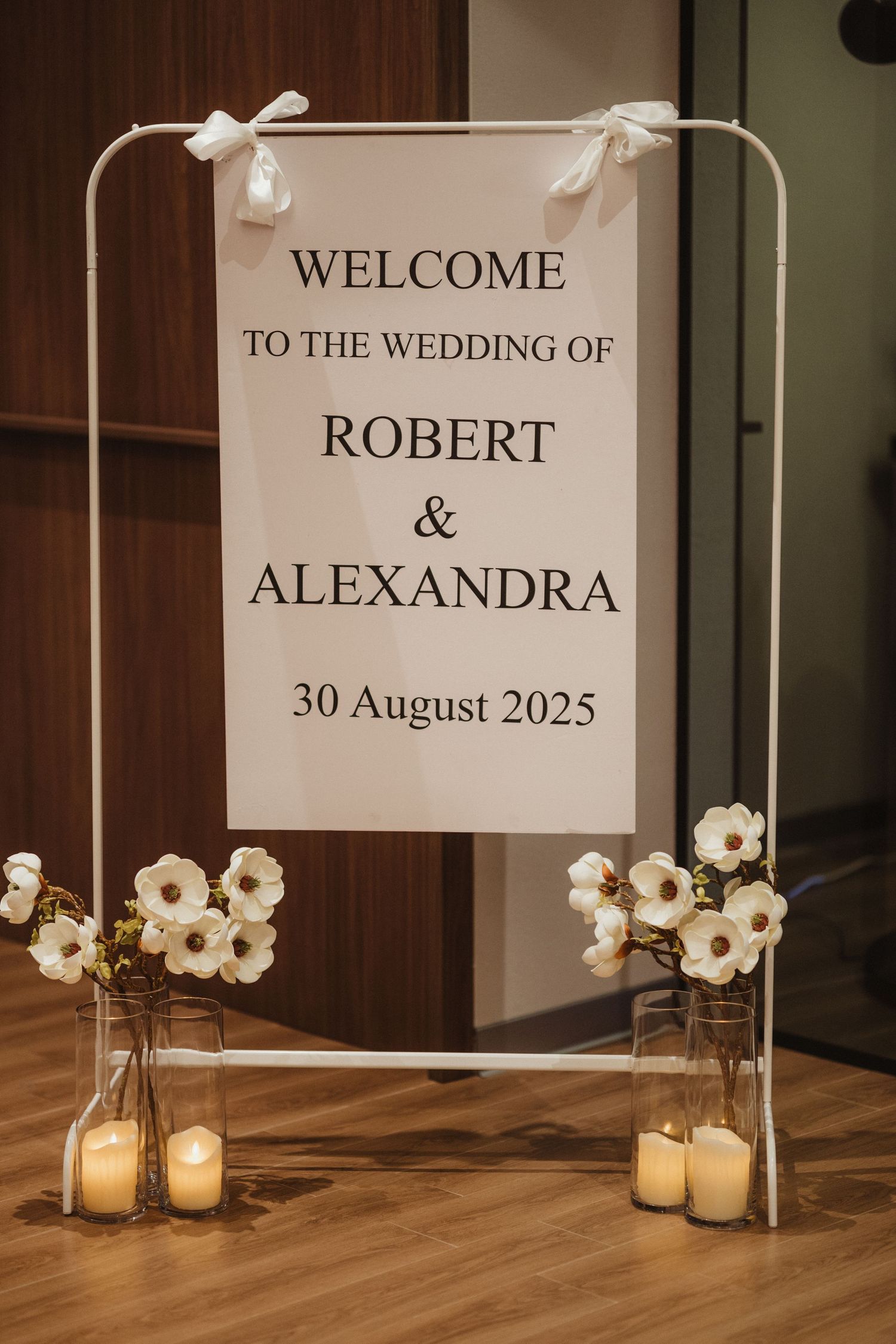 Elegant wedding welcome sign for Robert and Alexandra on 30 August 2025 with white flowers and candles.