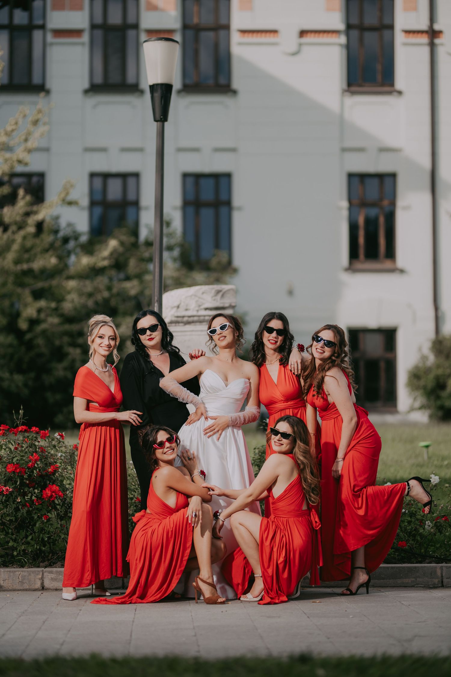 Bride with seven bridesmaids in red dresses posing outdoors near a historic building. Epicu Fotograf Drobeta-Turnu Severin