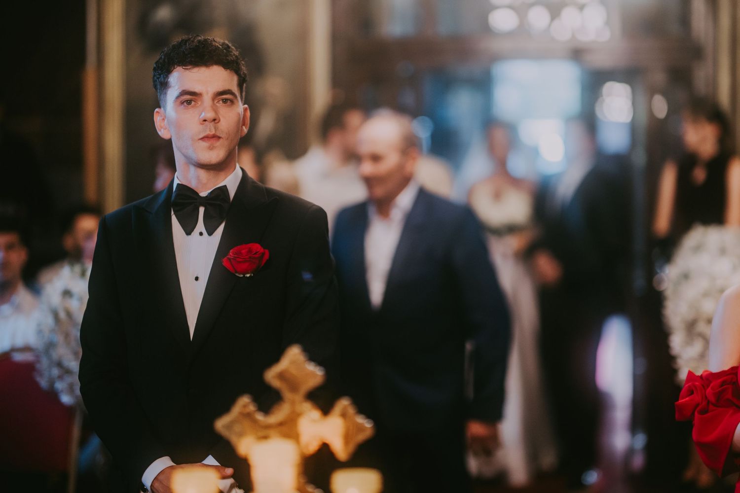 Groom in black tuxedo with red rose boutonniere stands at church altar during wedding ceremony. Epicu Fotograf Drobeta-Turnu Severin