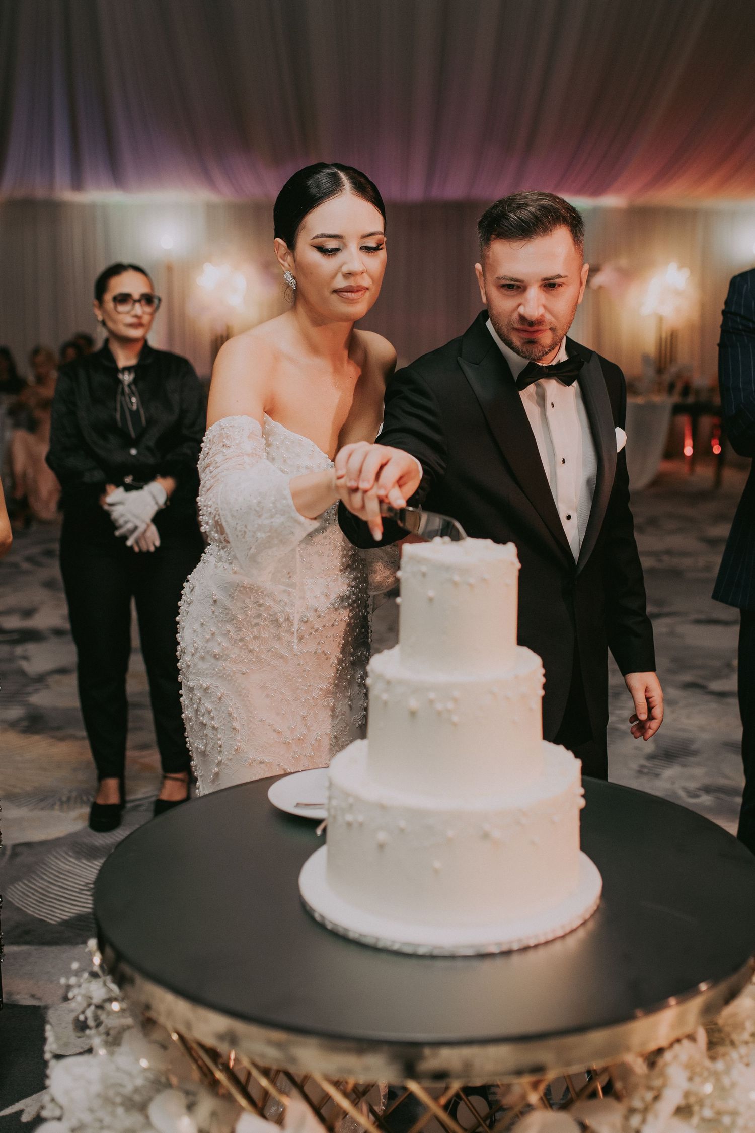 Bride and groom cut their elegant three-tier white wedding cake together at their reception celebration.