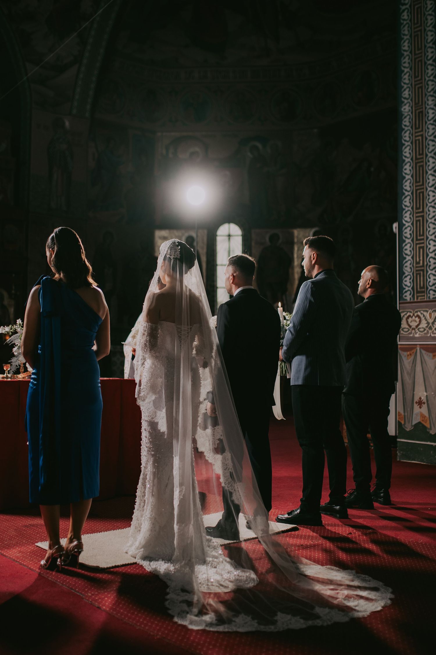 Bride and groom standing at altar in ornate Orthodox church with religious icons and dramatic lighting.