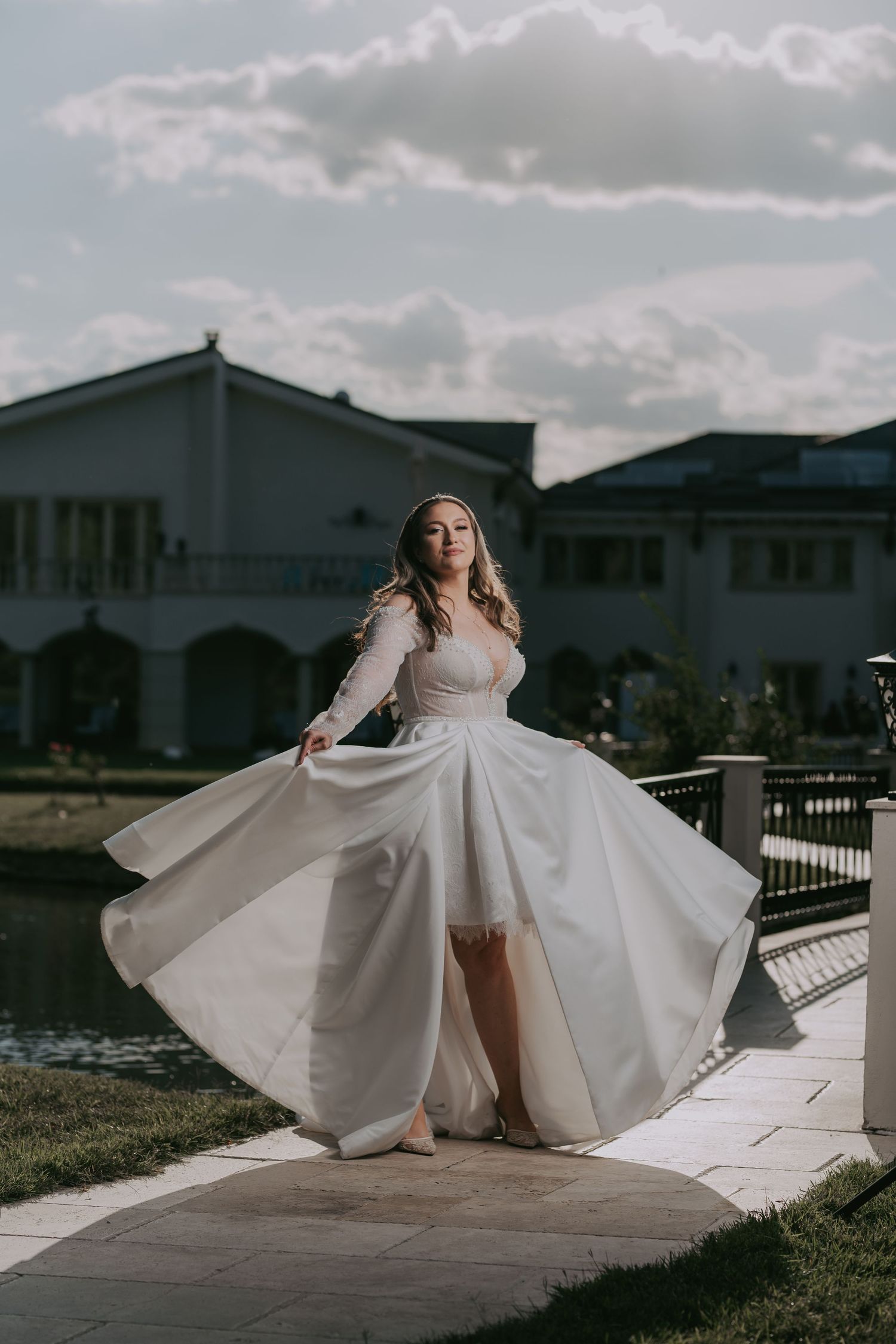 Bride twirls in stunning white ballgown with lace sleeves beside a scenic waterfront venue. Epicu Fotograf Drobeta-Turnu Severin