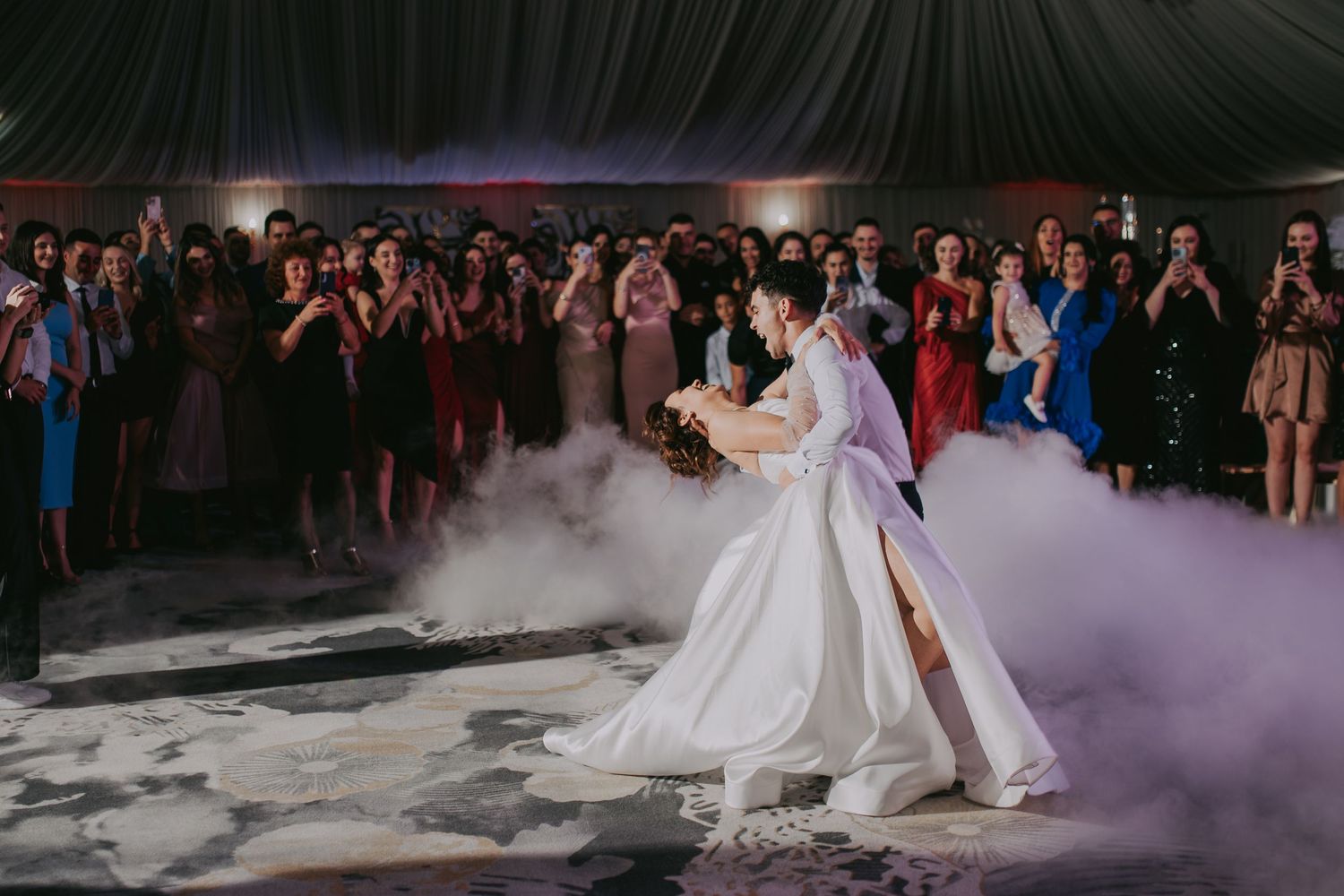 Bride in white gown dances on foggy floor as guests cheer and photograph at wedding reception. Epicu Fotograf Drobeta-Turnu Severin