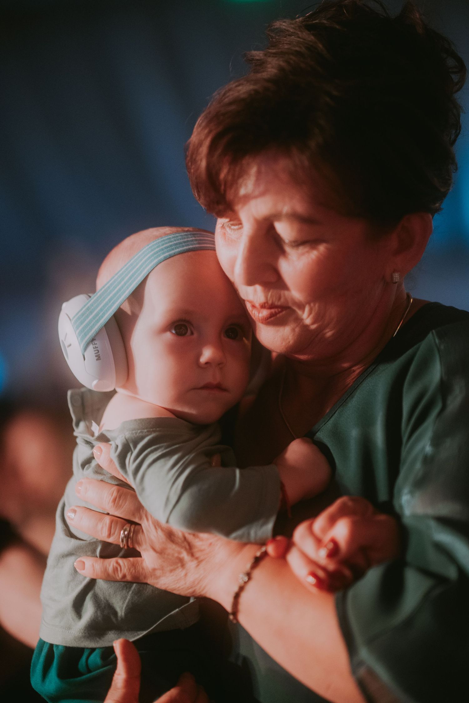 Grandmother tenderly holds baby with ear protection at a lively wedding reception. Epicu Fotograf Drobeta-Turnu Severin