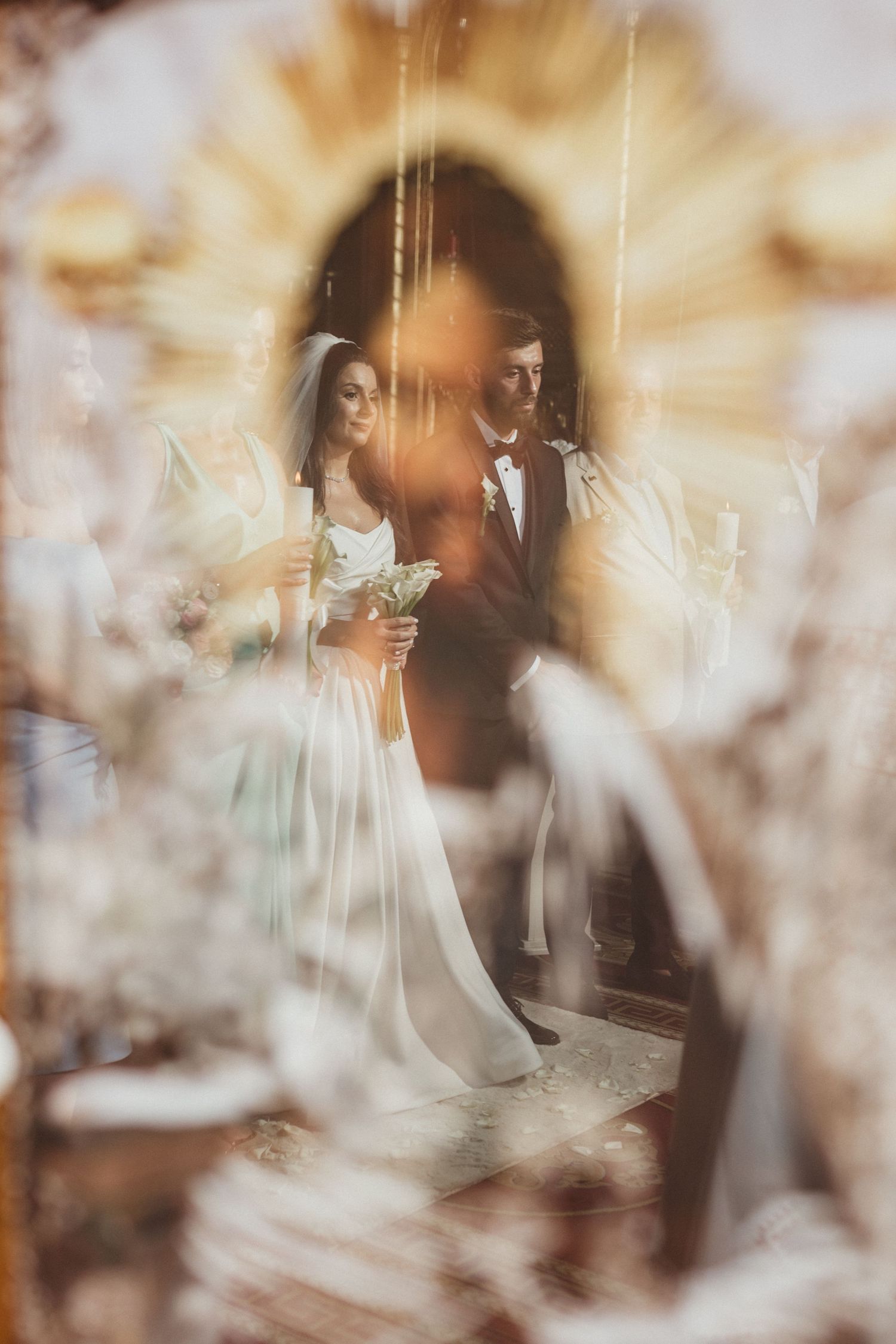 Bride and groom hold candles during a golden-lit church wedding ceremony reflection.