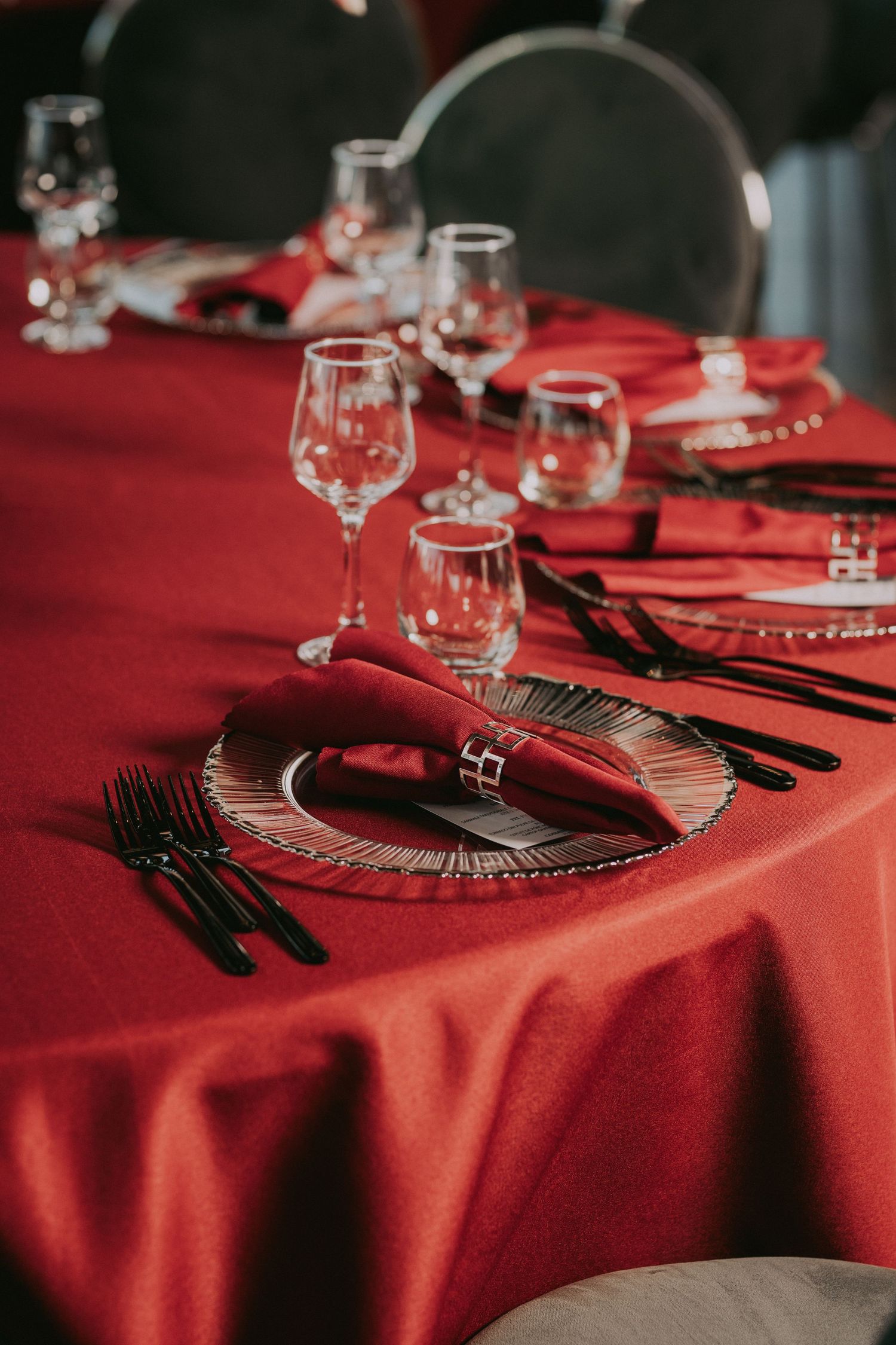 Elegant red wedding table setting with crystal glassware, black cutlery, and folded napkins on red cloth.