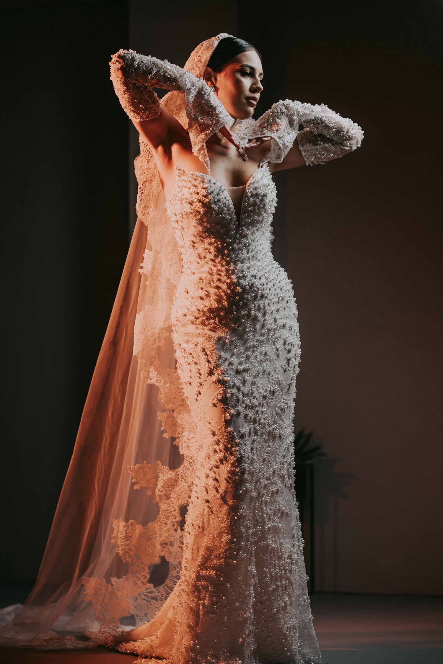 Bride in floral 3D embellished mermaid gown with sheer veil in dramatic light.