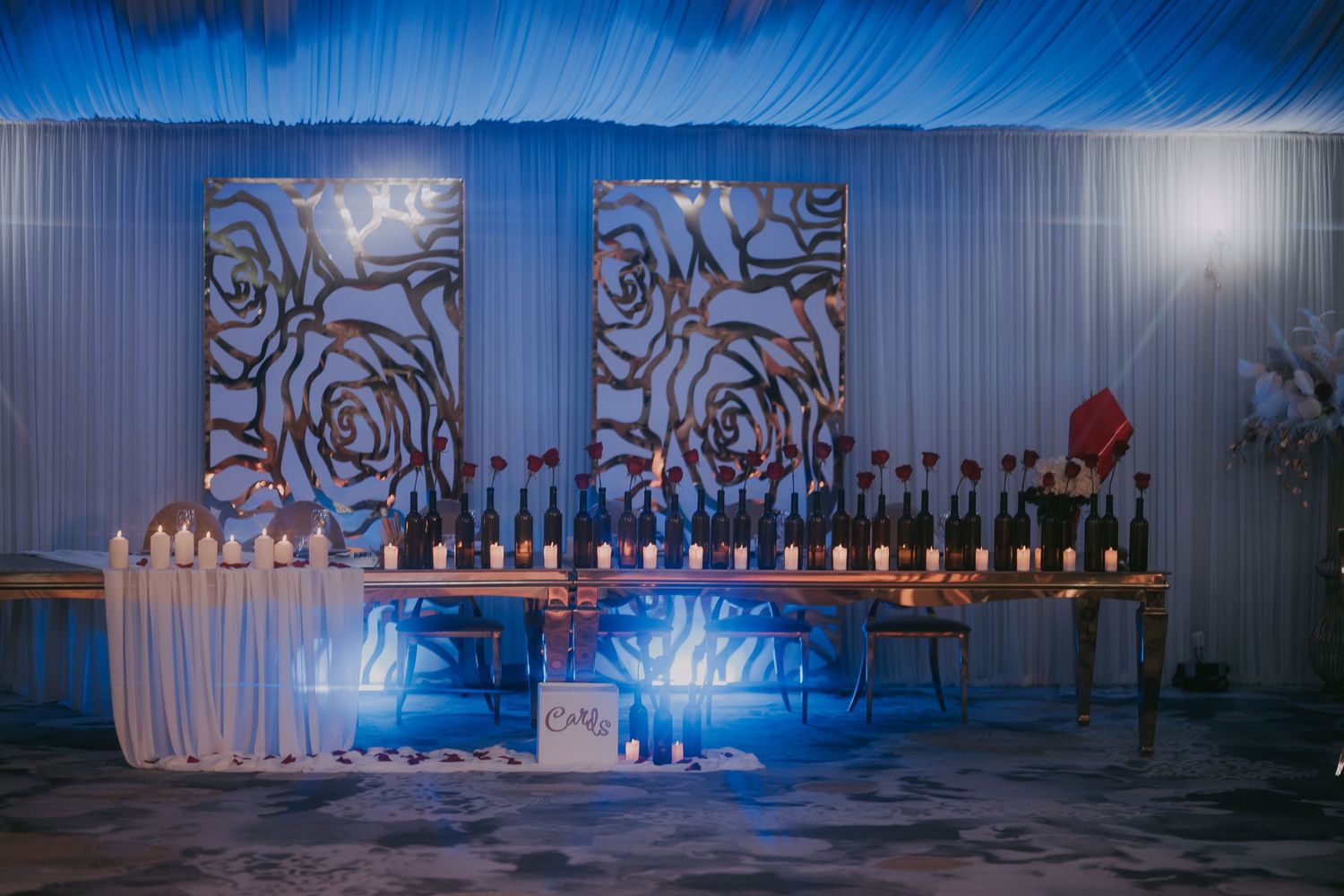 Dramatic blue-lit wedding bar setup with rose panel backdrop, wine bottles, and white draping. Epicu Fotograf Drobeta-Turnu Severin