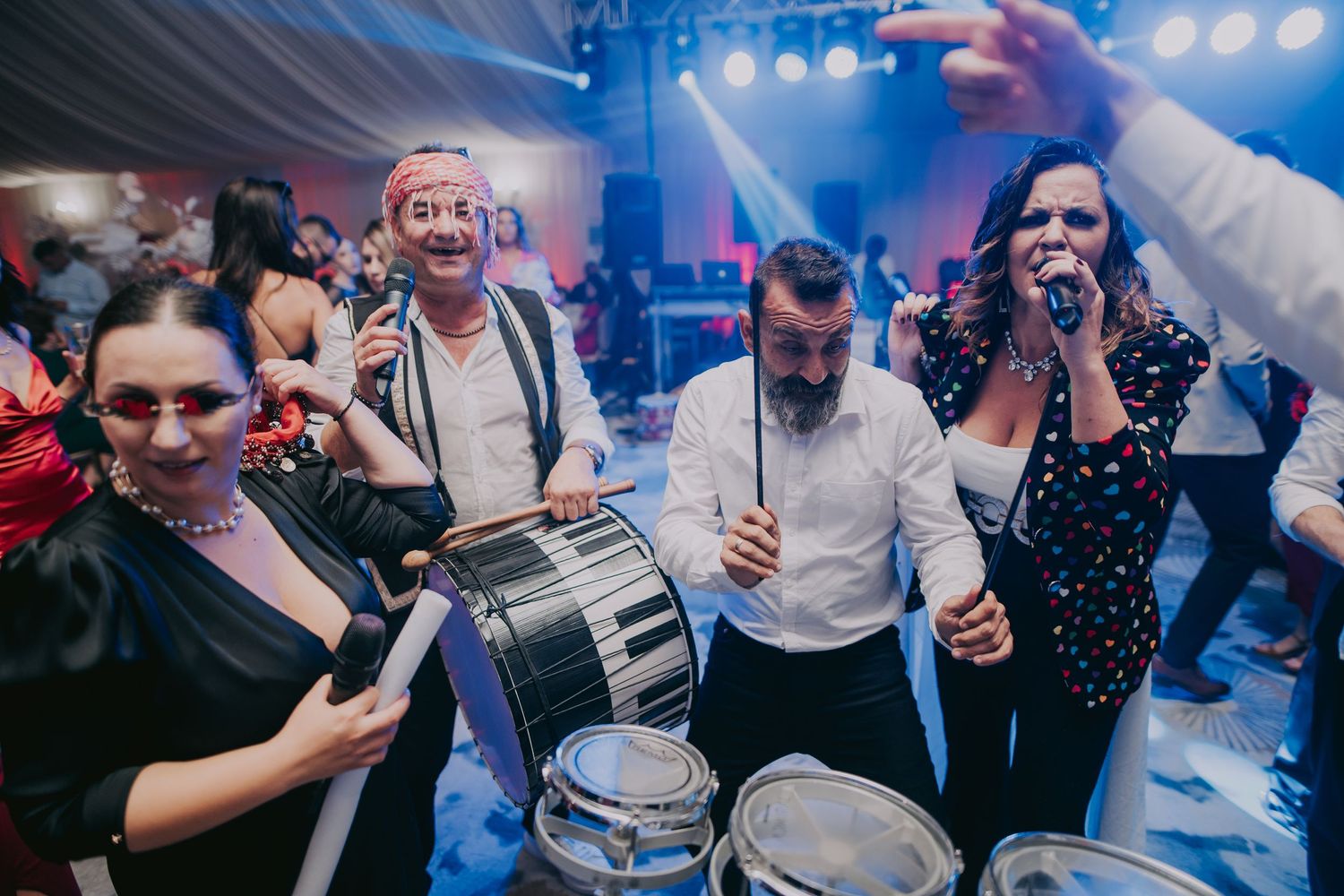 Live wedding band performing with drums and vocalist in colorful outfits at a festive reception. Epicu Fotograf Drobeta-Turnu Severin