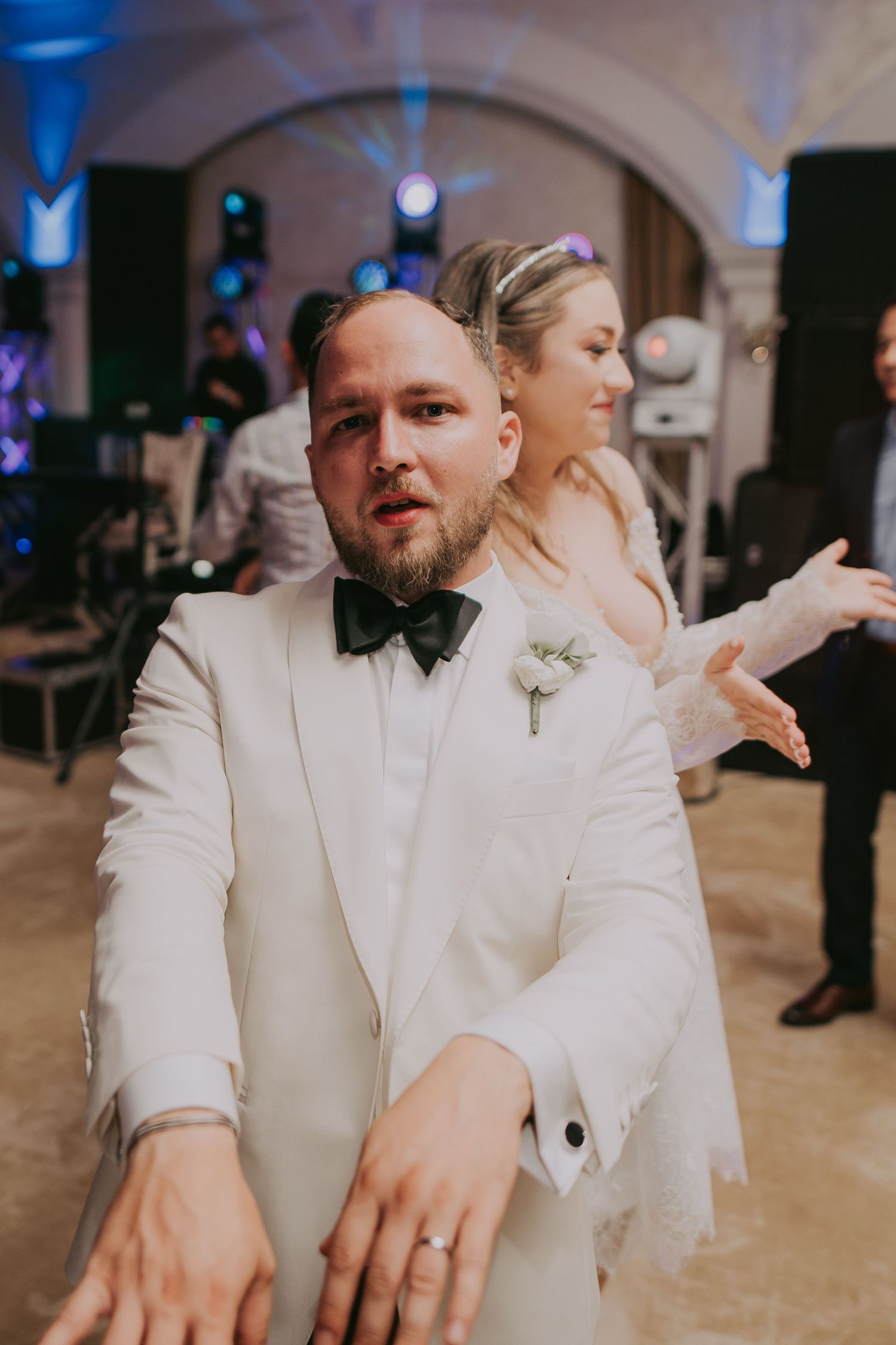 Groom in white tuxedo dancing with bride in background at elegant wedding reception venue. Epicu Fotograf Drobeta-Turnu Severin