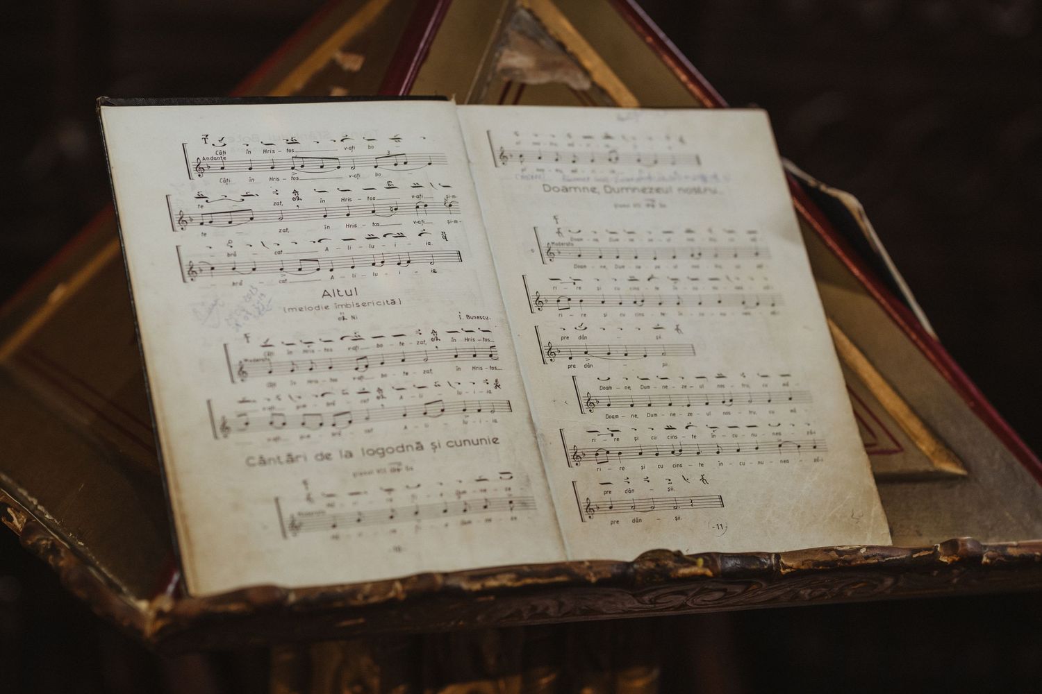 Vintage open hymn book with sheet music displayed on a wooden stand inside an Orthodox church.