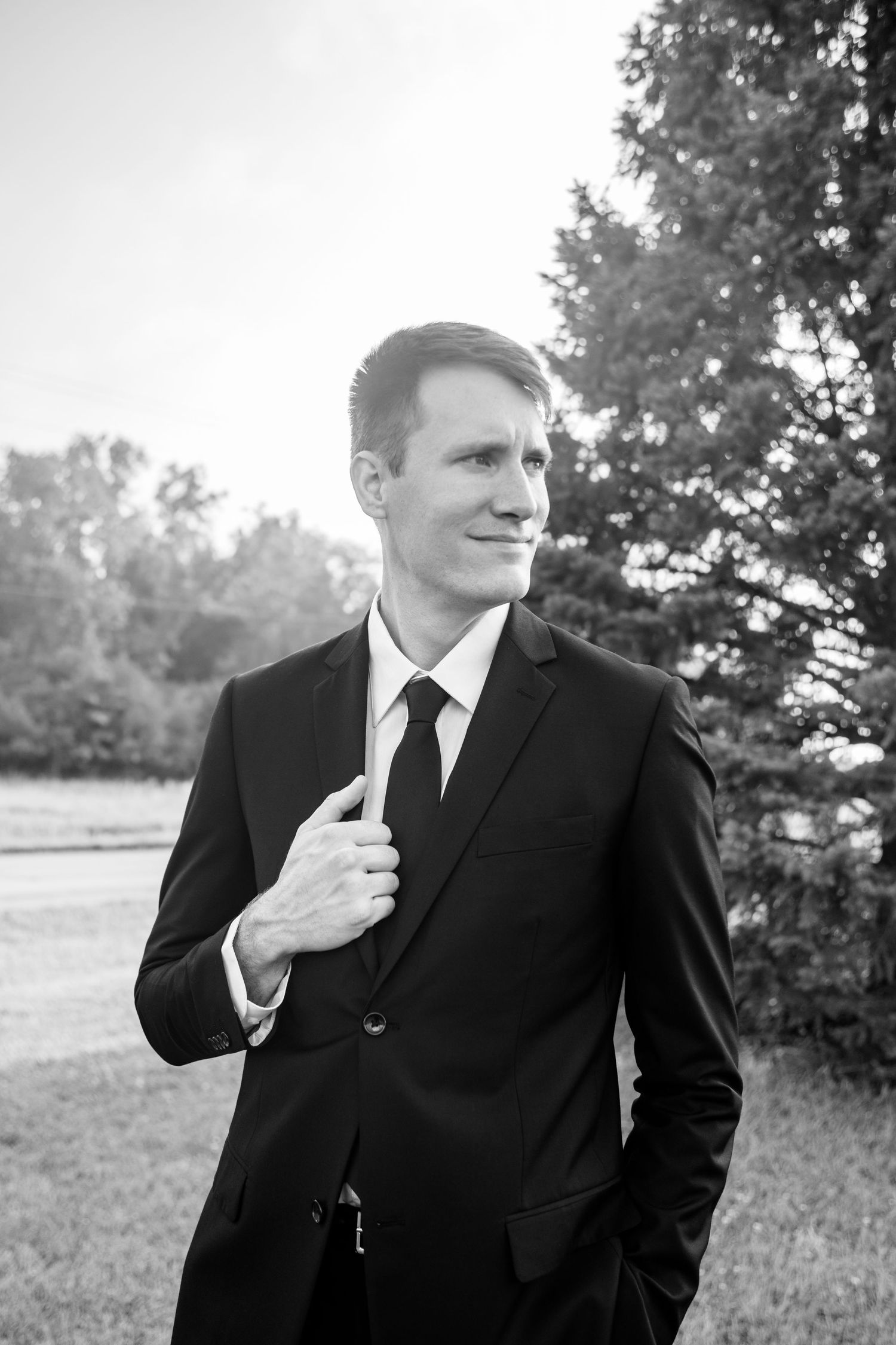 Elegant groom in black suit and tie posing outdoors in black and white portrait.