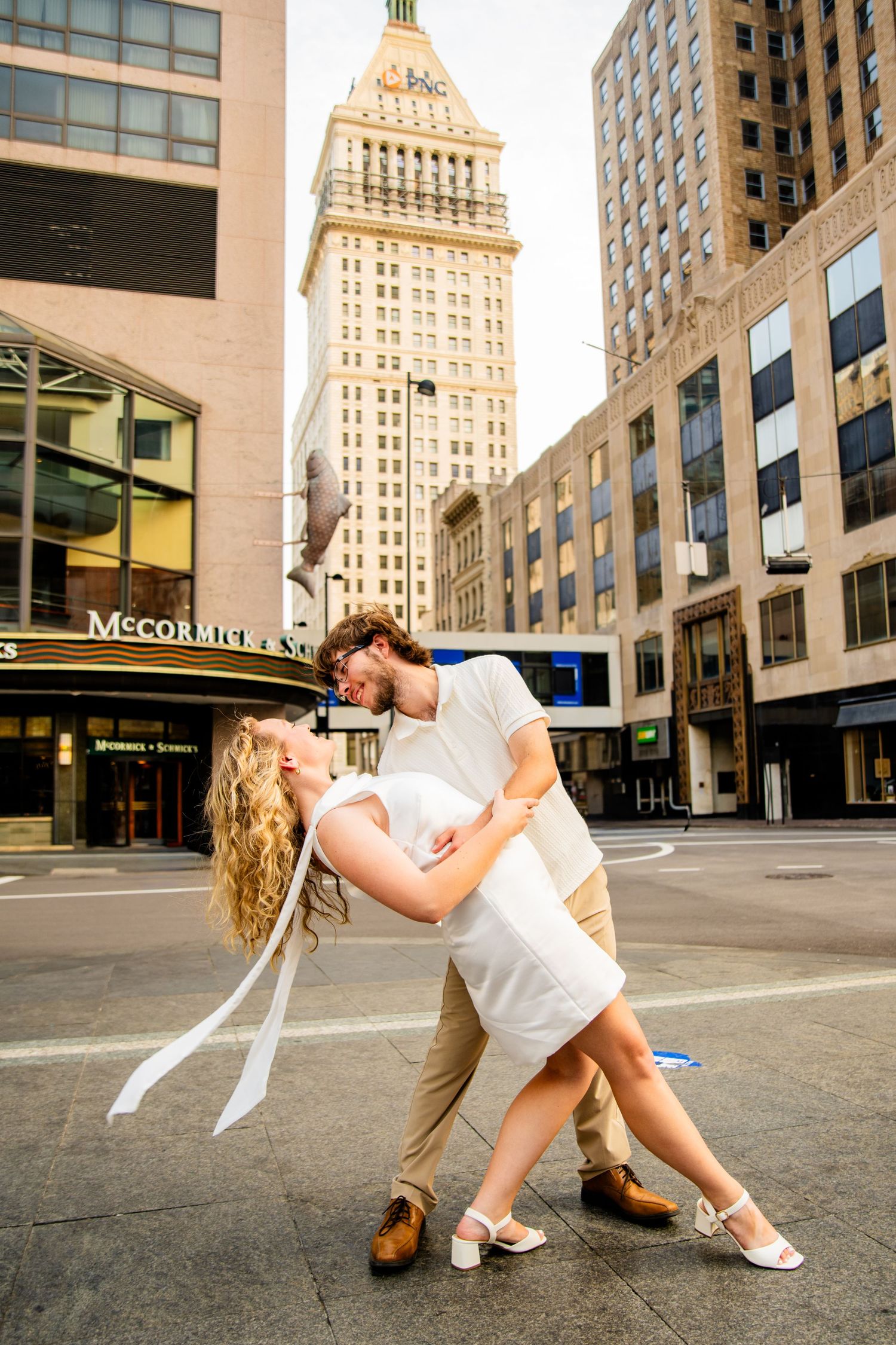 Couple sharing a romantic dip kiss in an urban cityscape with tall buildings and McCormick sign in background.