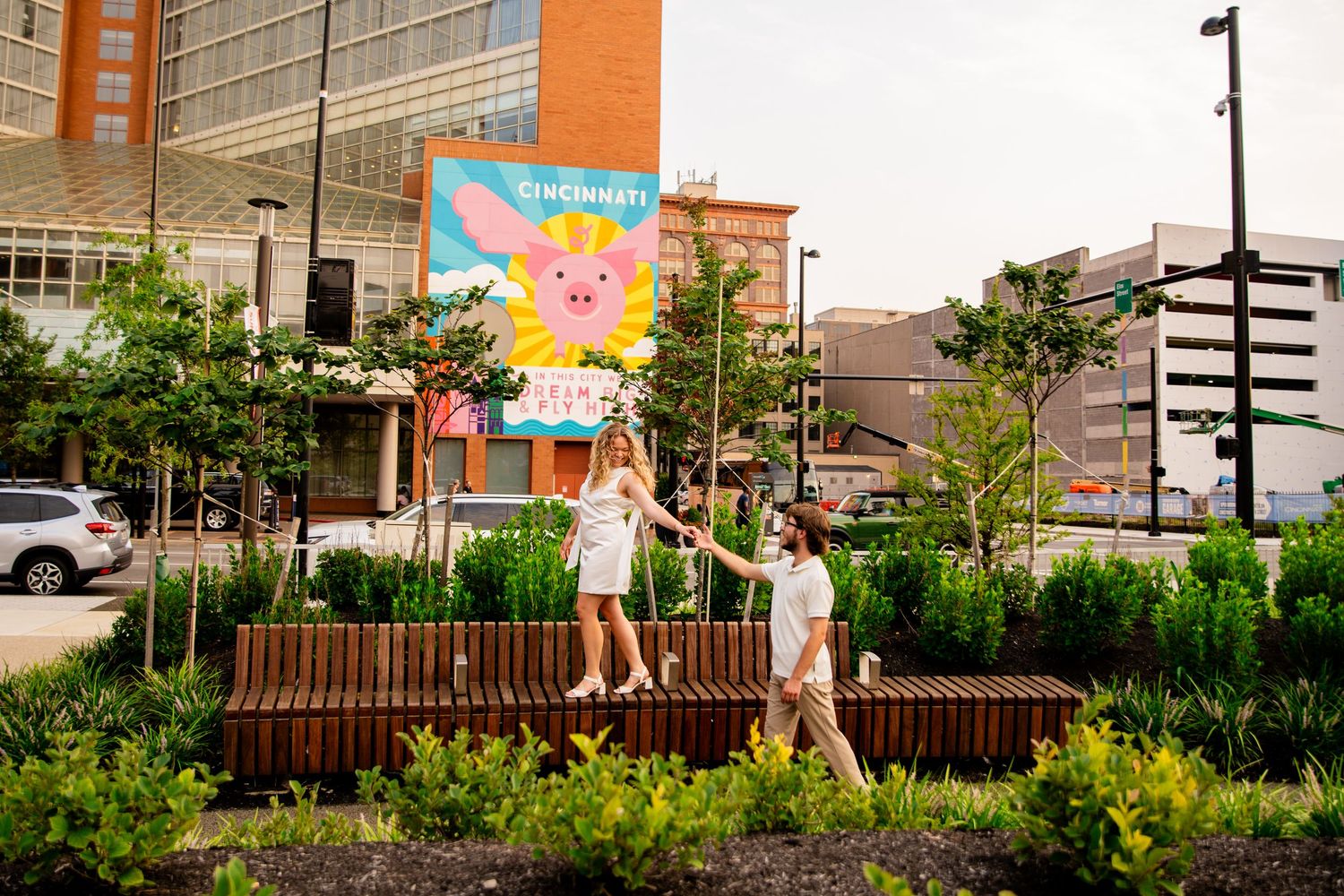 Couple holding hands and strolling through a city garden with a vibrant pig mural visible behind them.