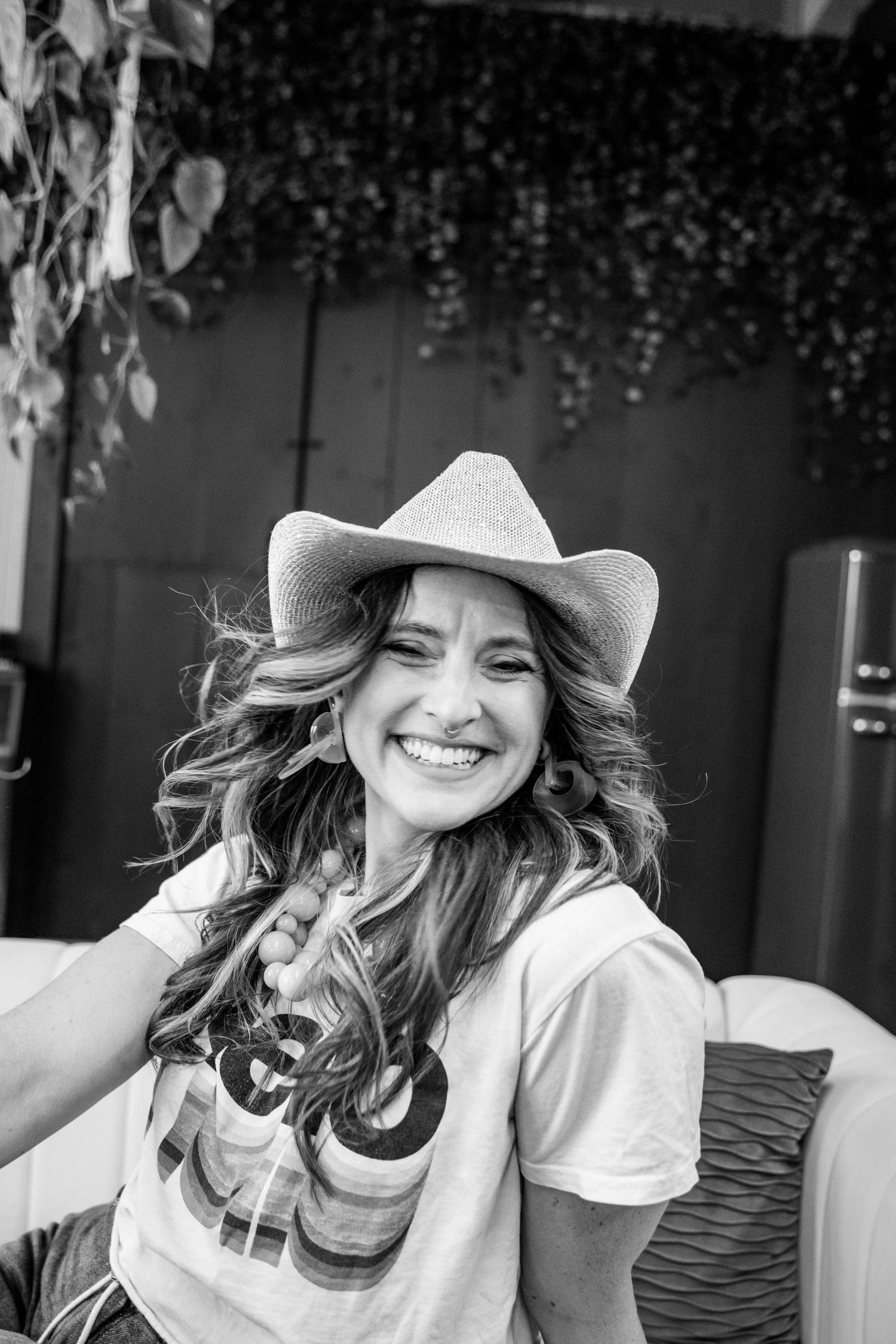 Smiling woman in cowboy hat and graphic tee laughing in black and white outdoor portrait photo.