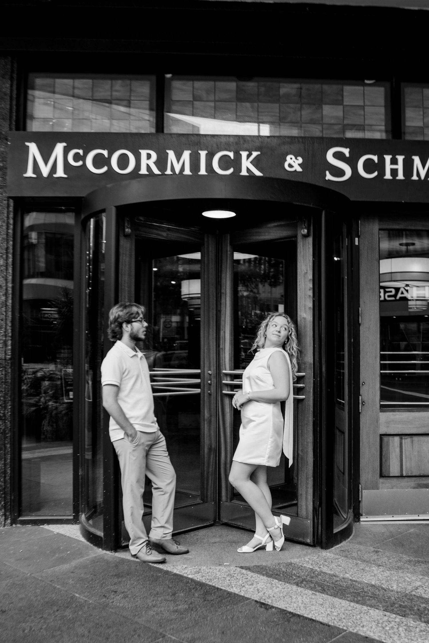 Black and white photo of a couple posing at McCormick & Schmick's revolving door entrance on a city street.