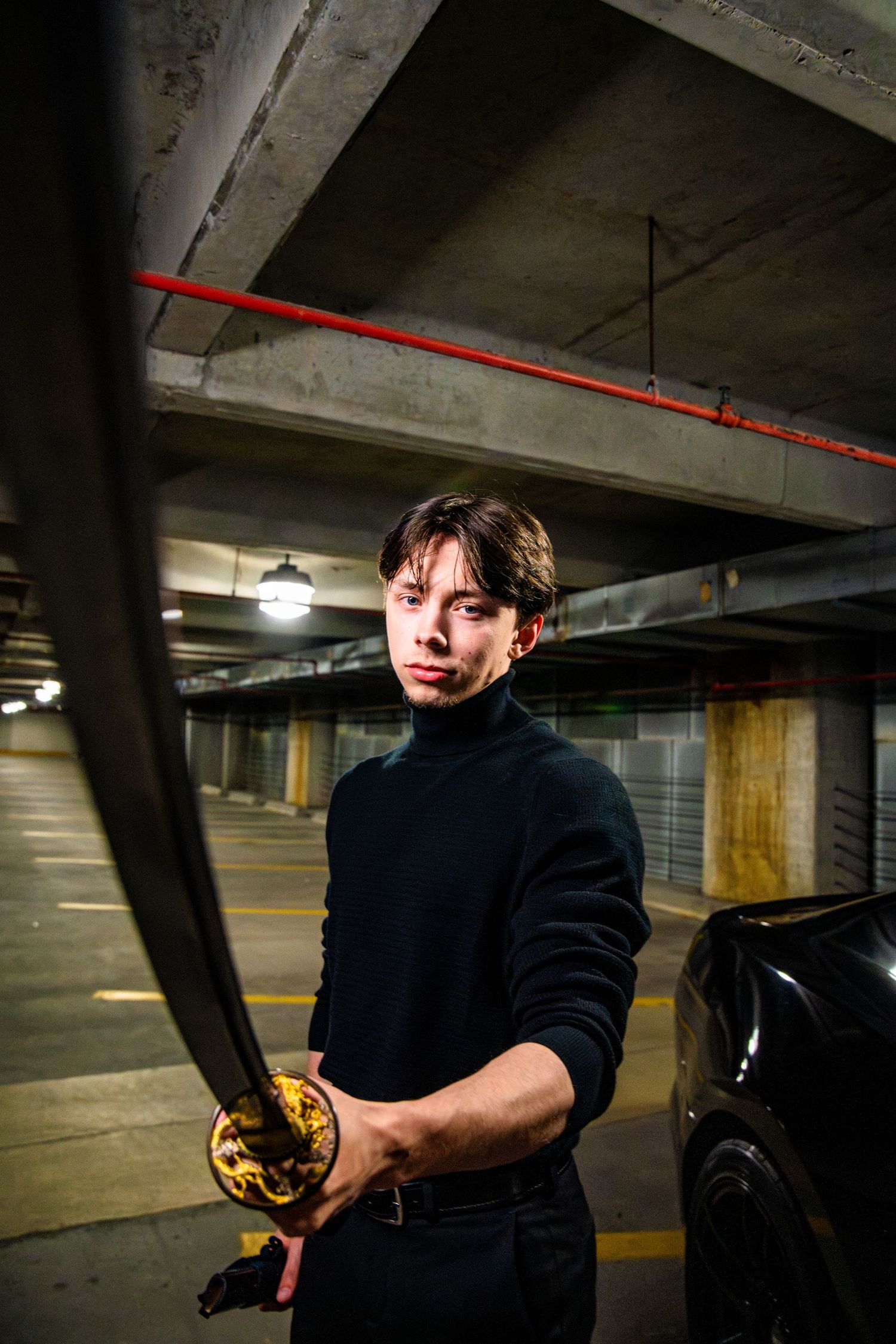 Cincinnati Young man in black turtleneck holding a katana sword in a dimly lit underground parking garage.