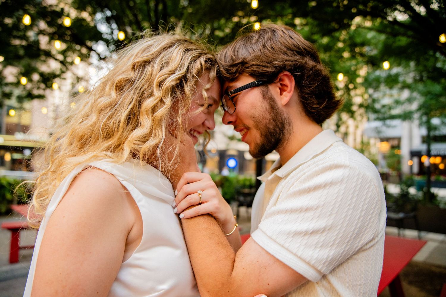 Happy couple holding hands and touching foreheads in a romantic outdoor urban setting.