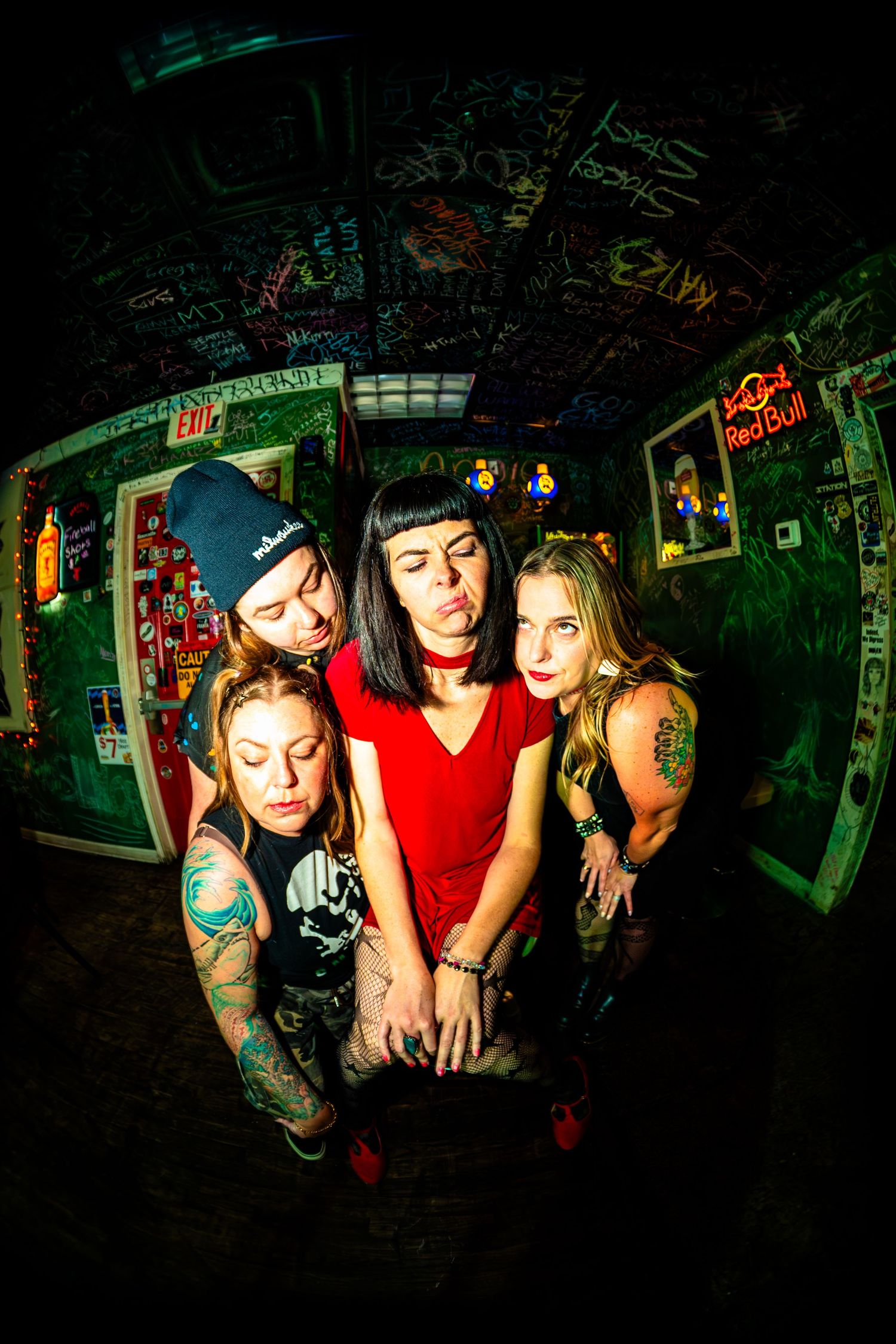 Four tattooed punk women pose dramatically in a graffiti-covered room under dim lighting with a Red Bull sign.