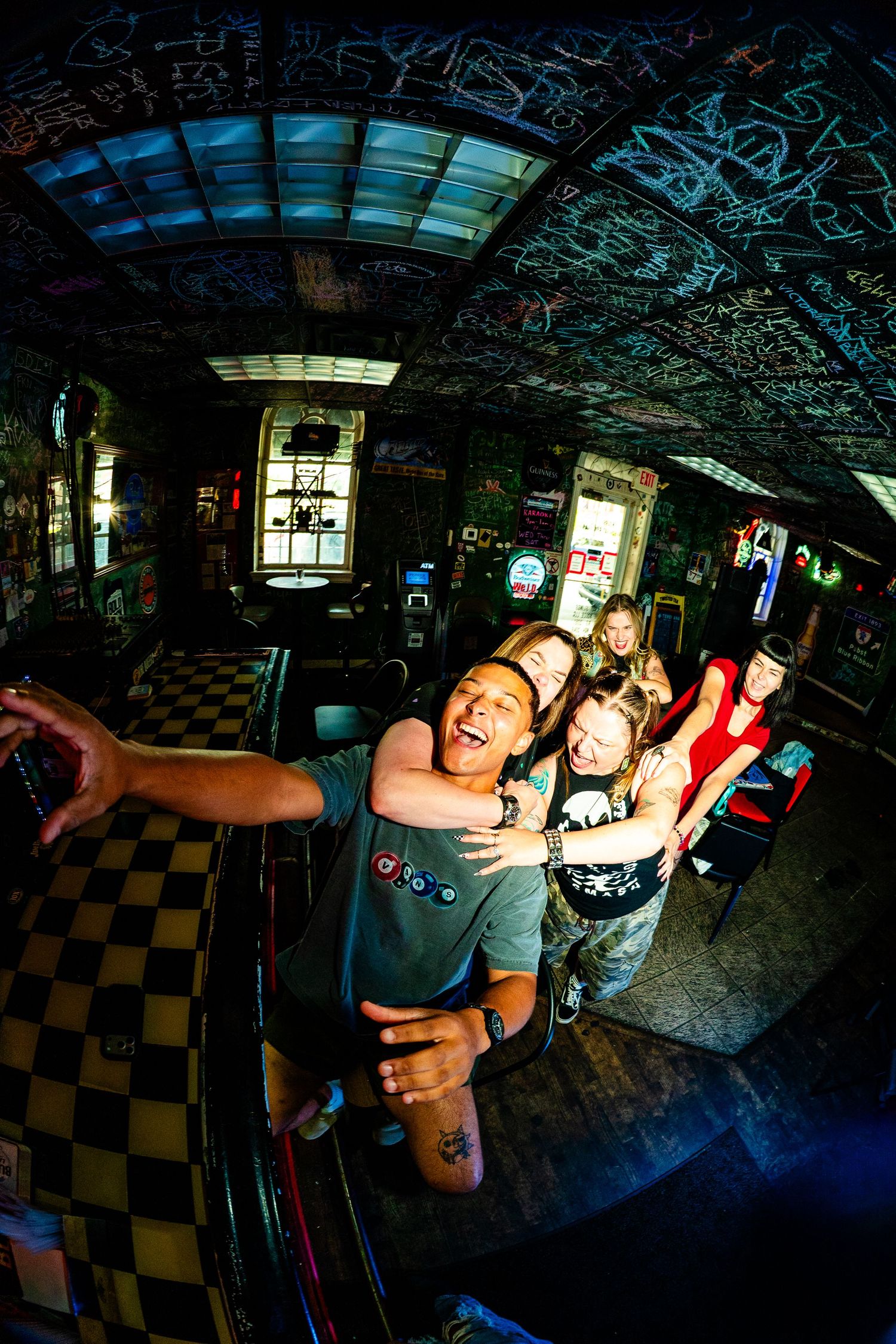 Group of friends taking a fun selfie inside a graffiti-covered rock bar with checkered floors.