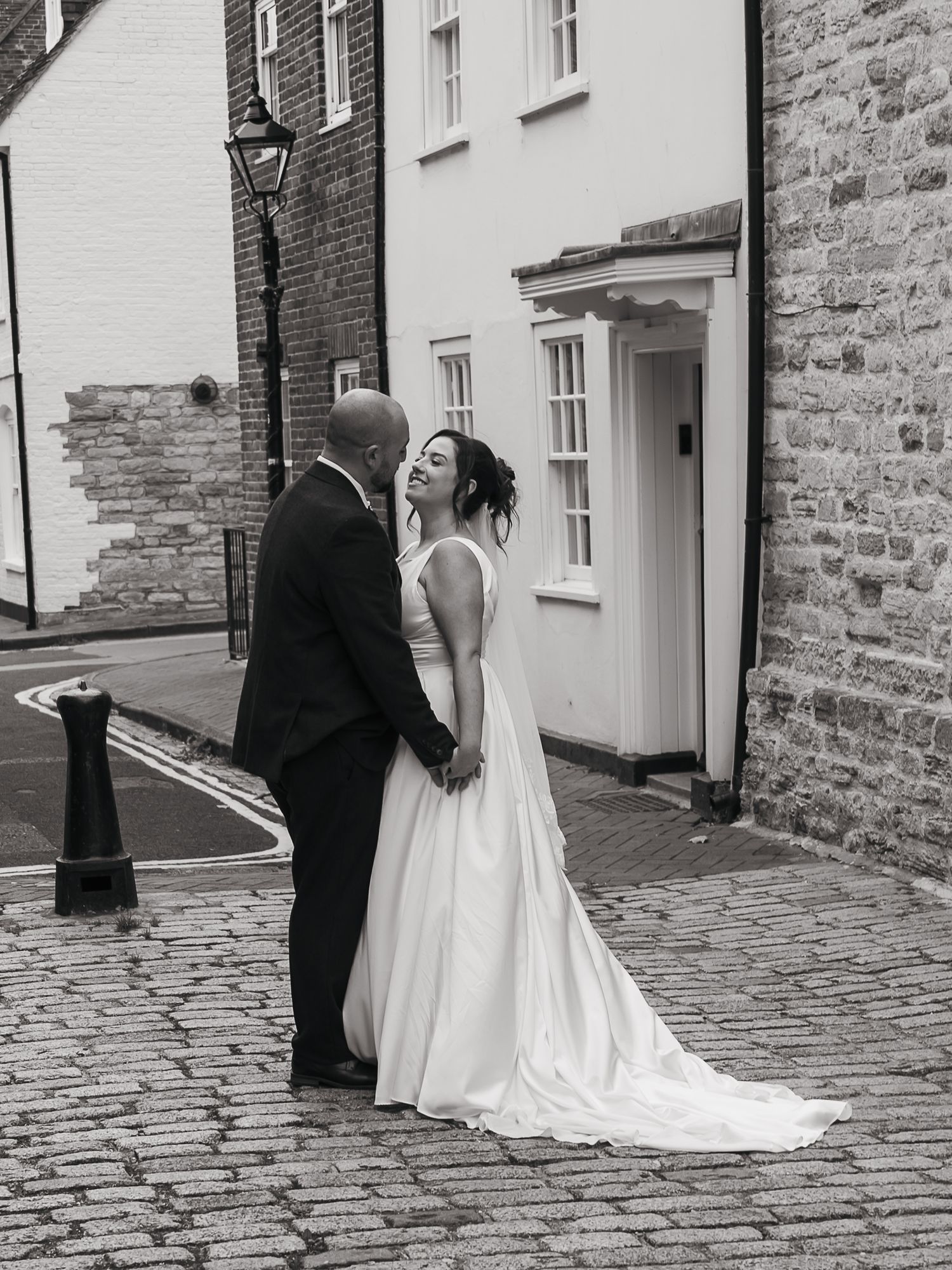Bride and groom looking at each other down cobbled street in Poole
