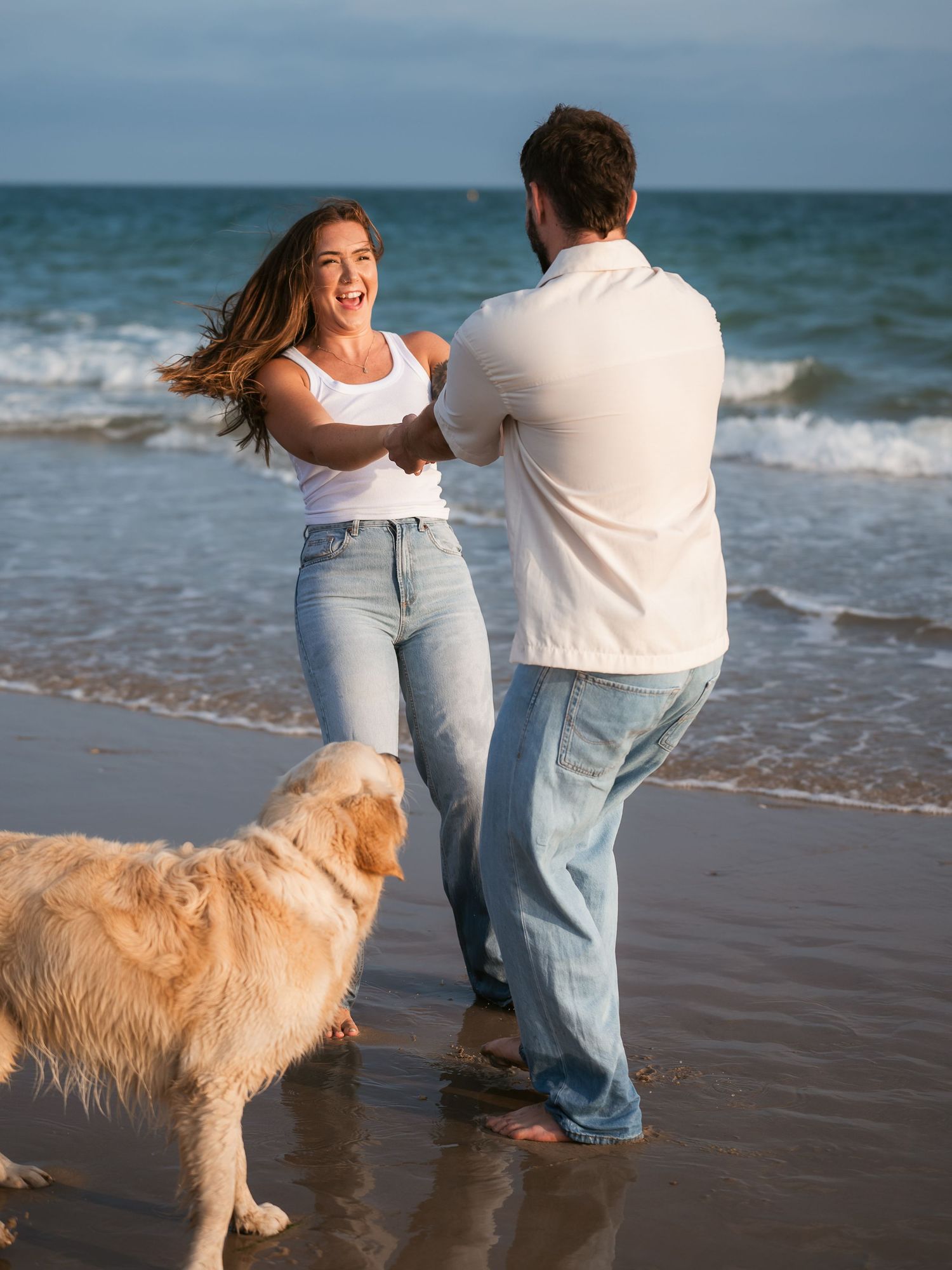 Couple playing at the beach with their dog at golden hour