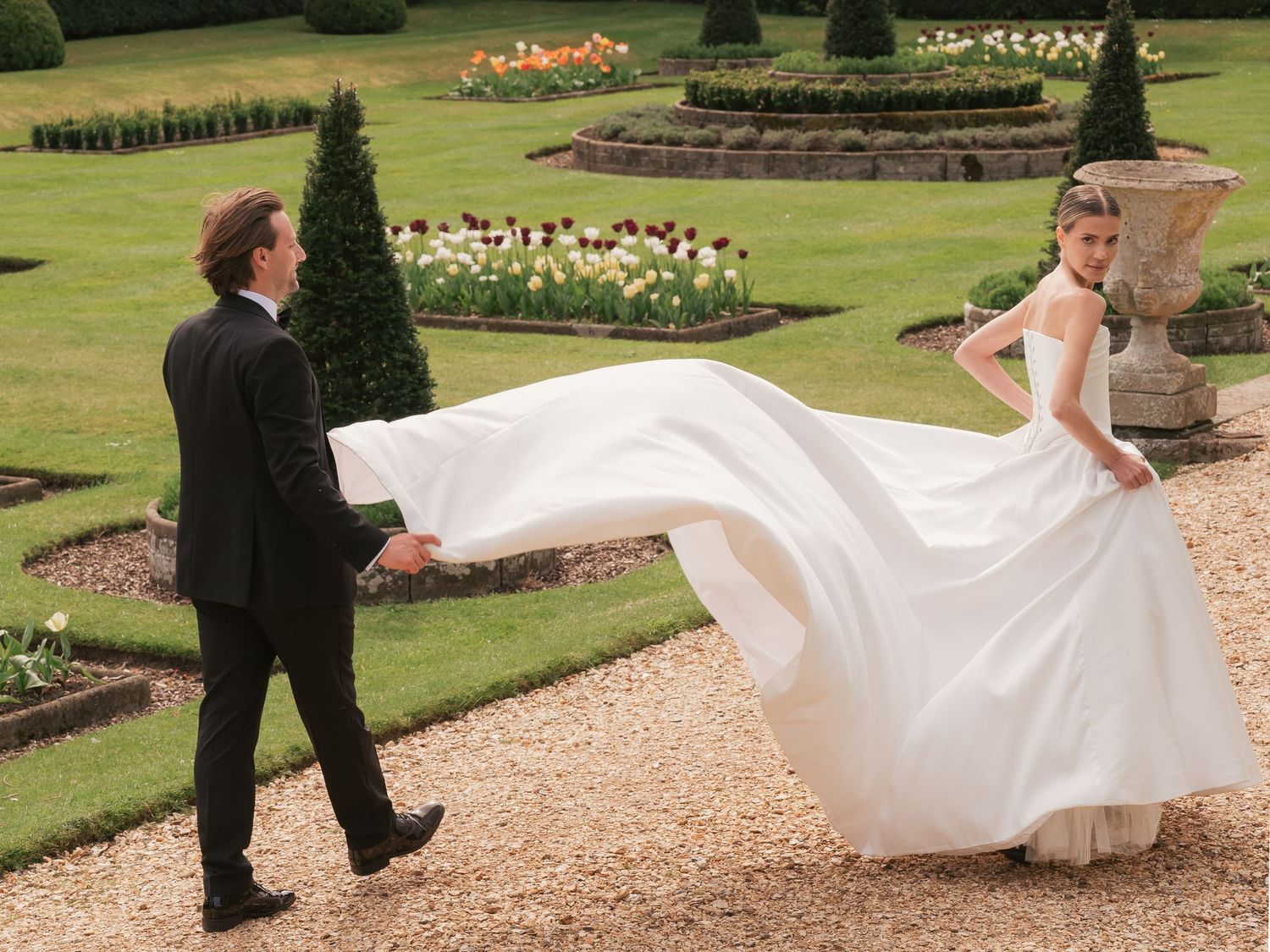 Bride and groom walking down path holding dress