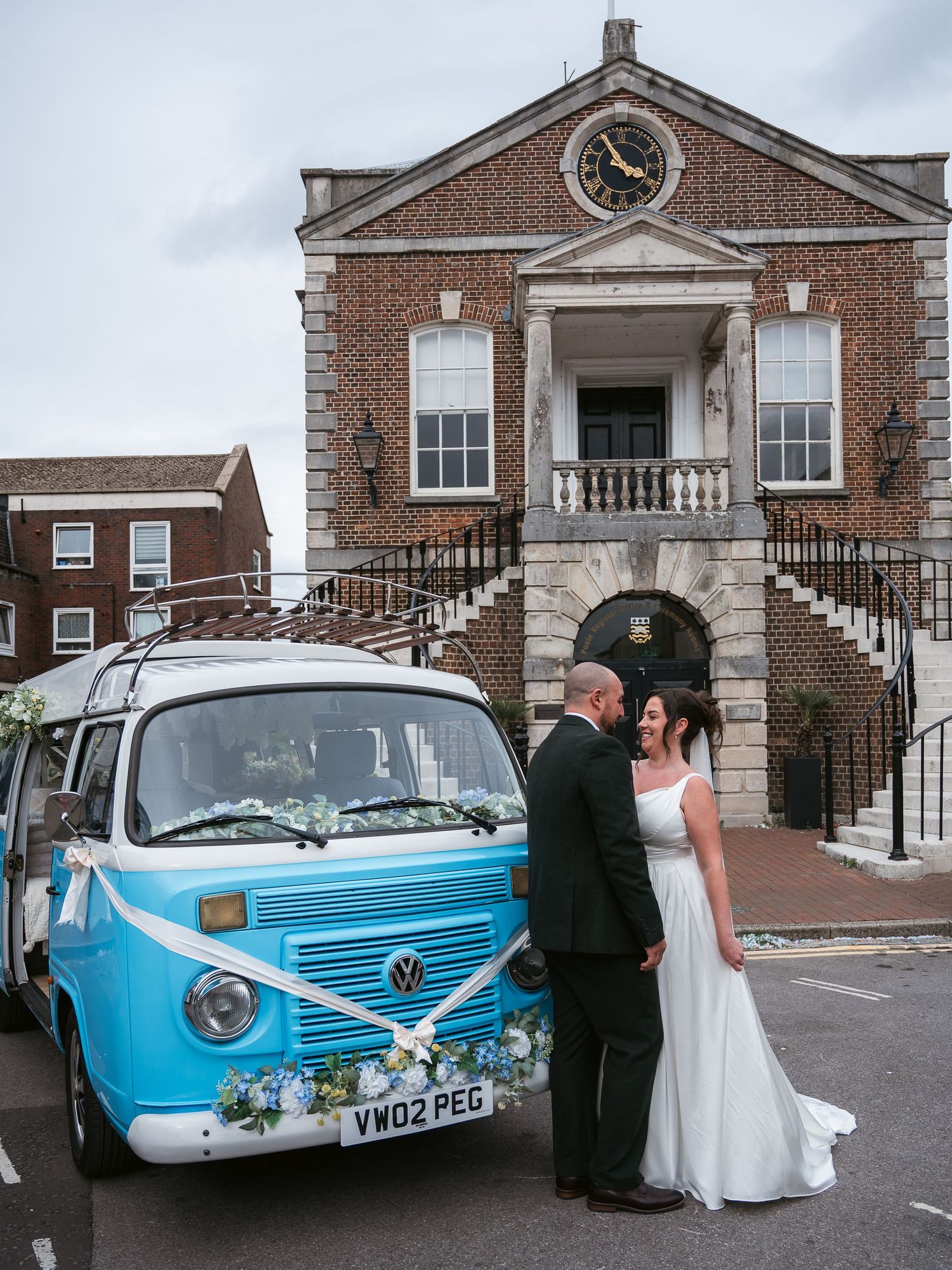 Bride and groom in front of registry office and standing next to their campervan