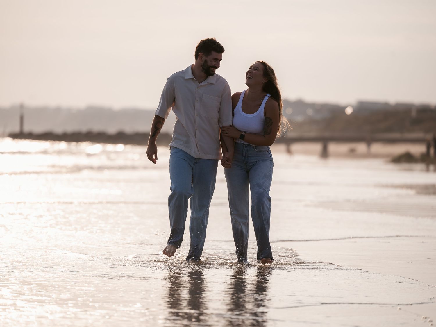 Newly engaged couple walking along beach at golden hour