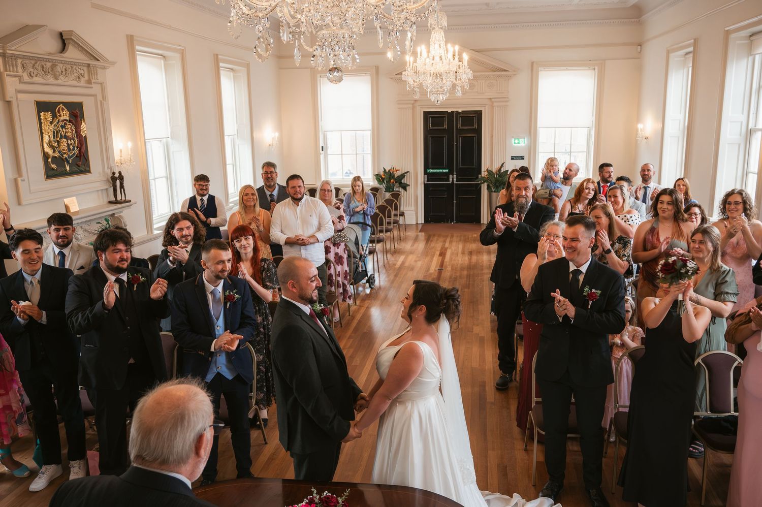 Bride and groom getting married in ceremony room with celebrating guests surrounding them