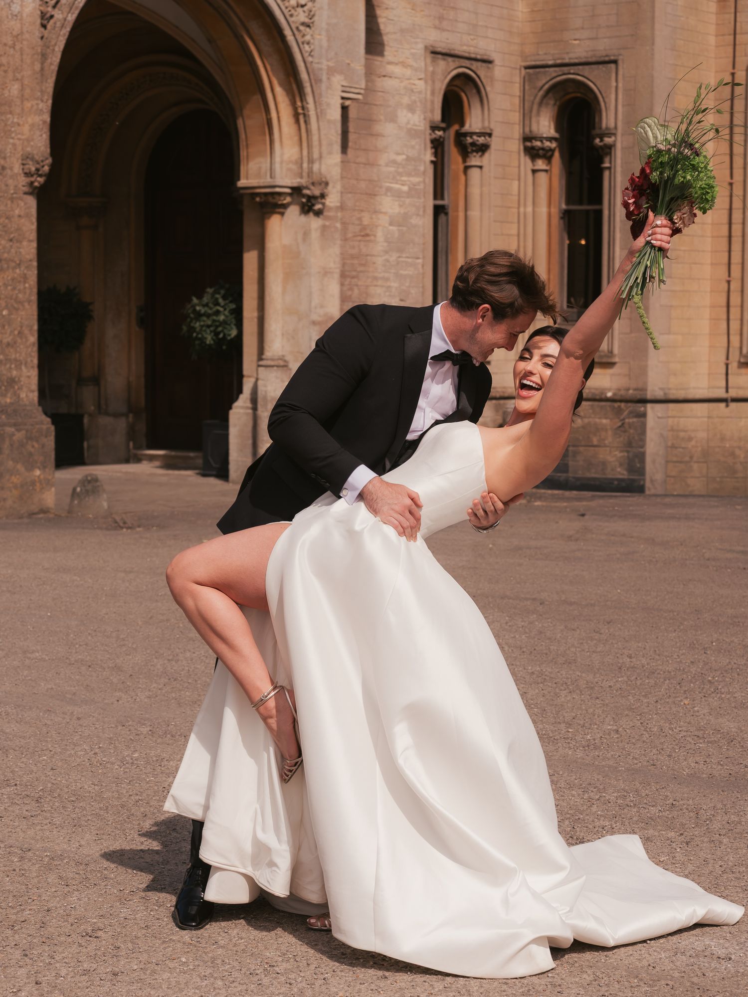 bride and groom dip shot while bride celebrates with bouquet in air