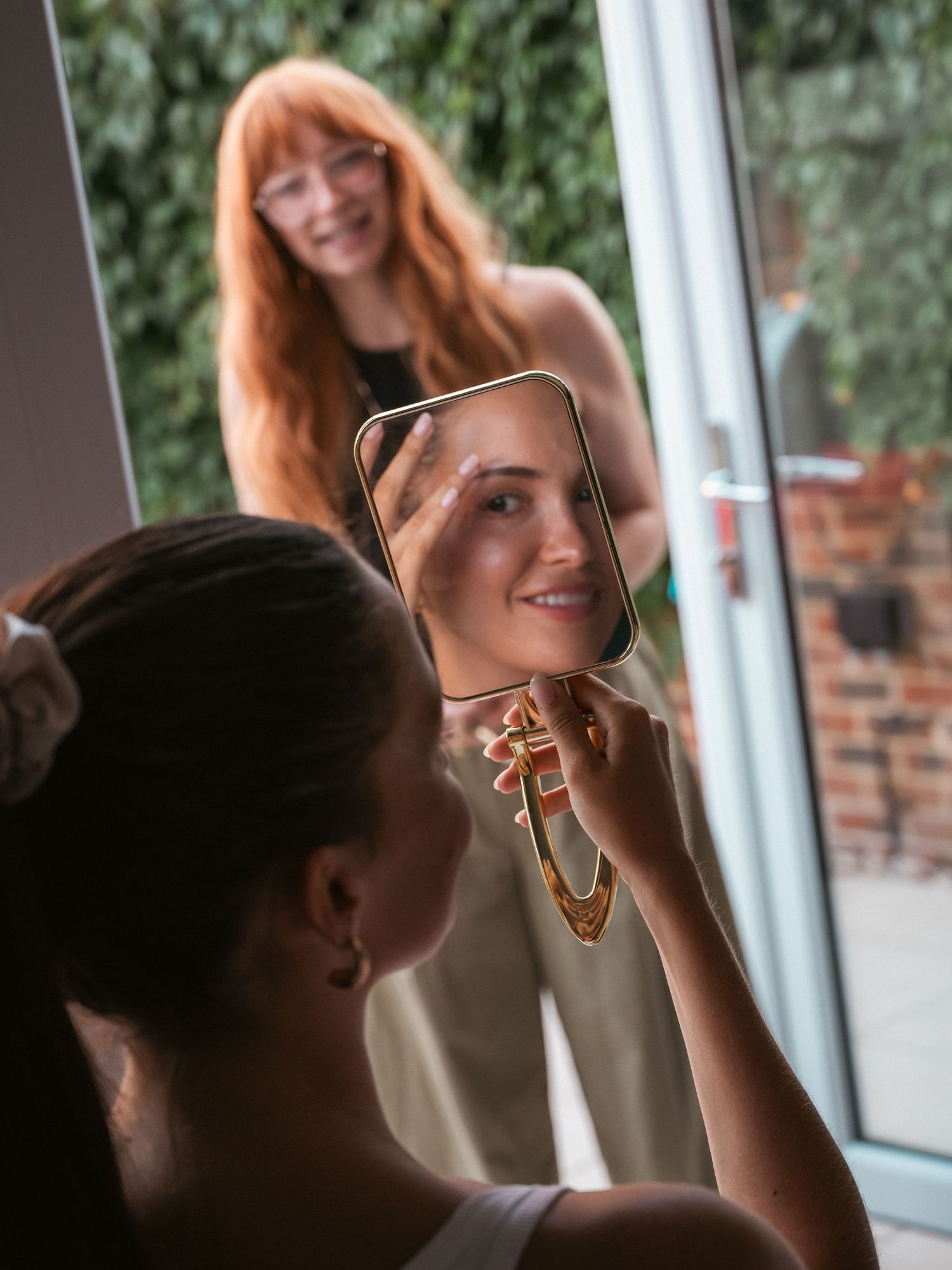 Model checking make up in mirror with MUA in background smiling