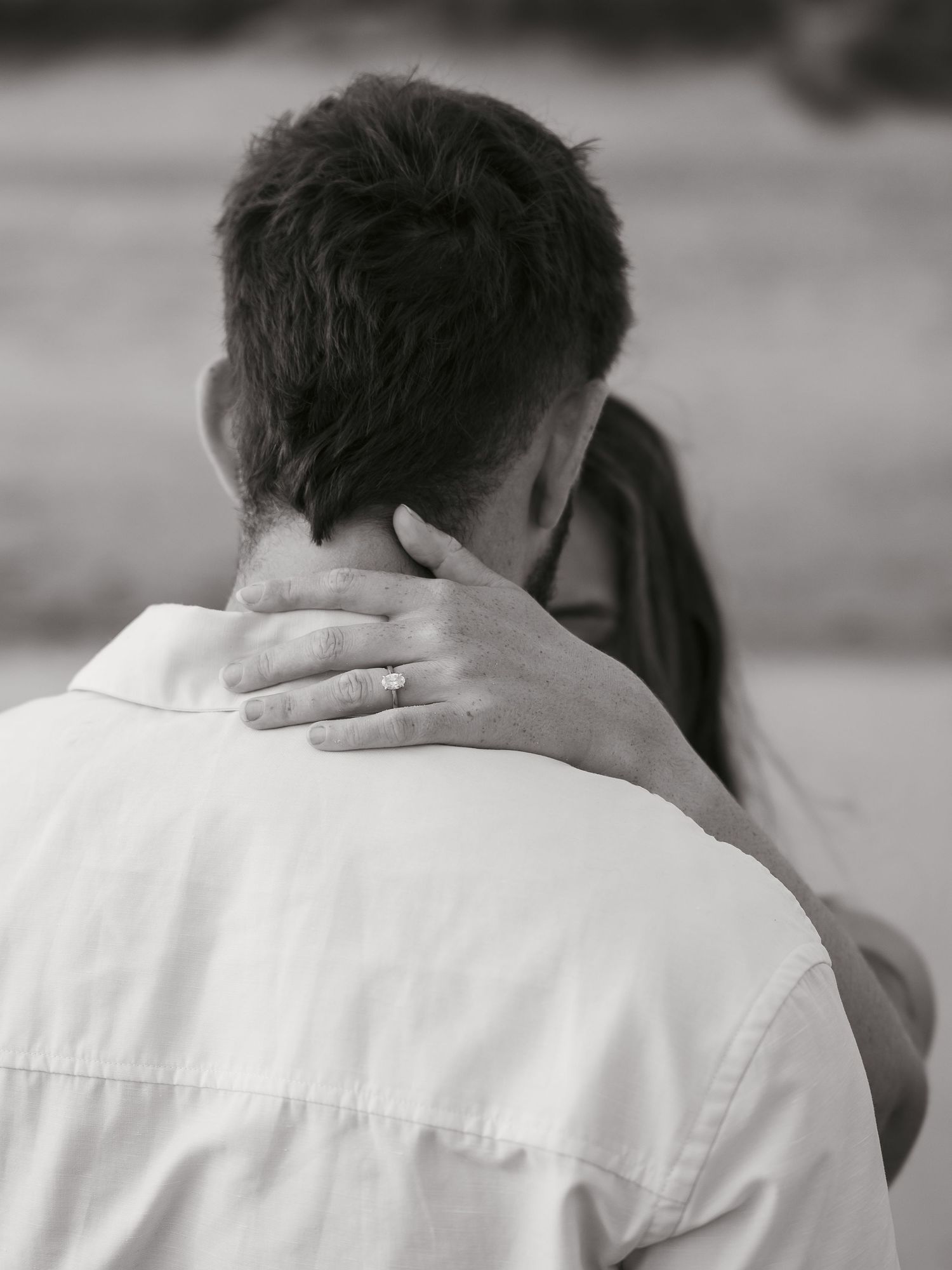Newly engaged couple embracing, ring seen on hand holding fiance's neck