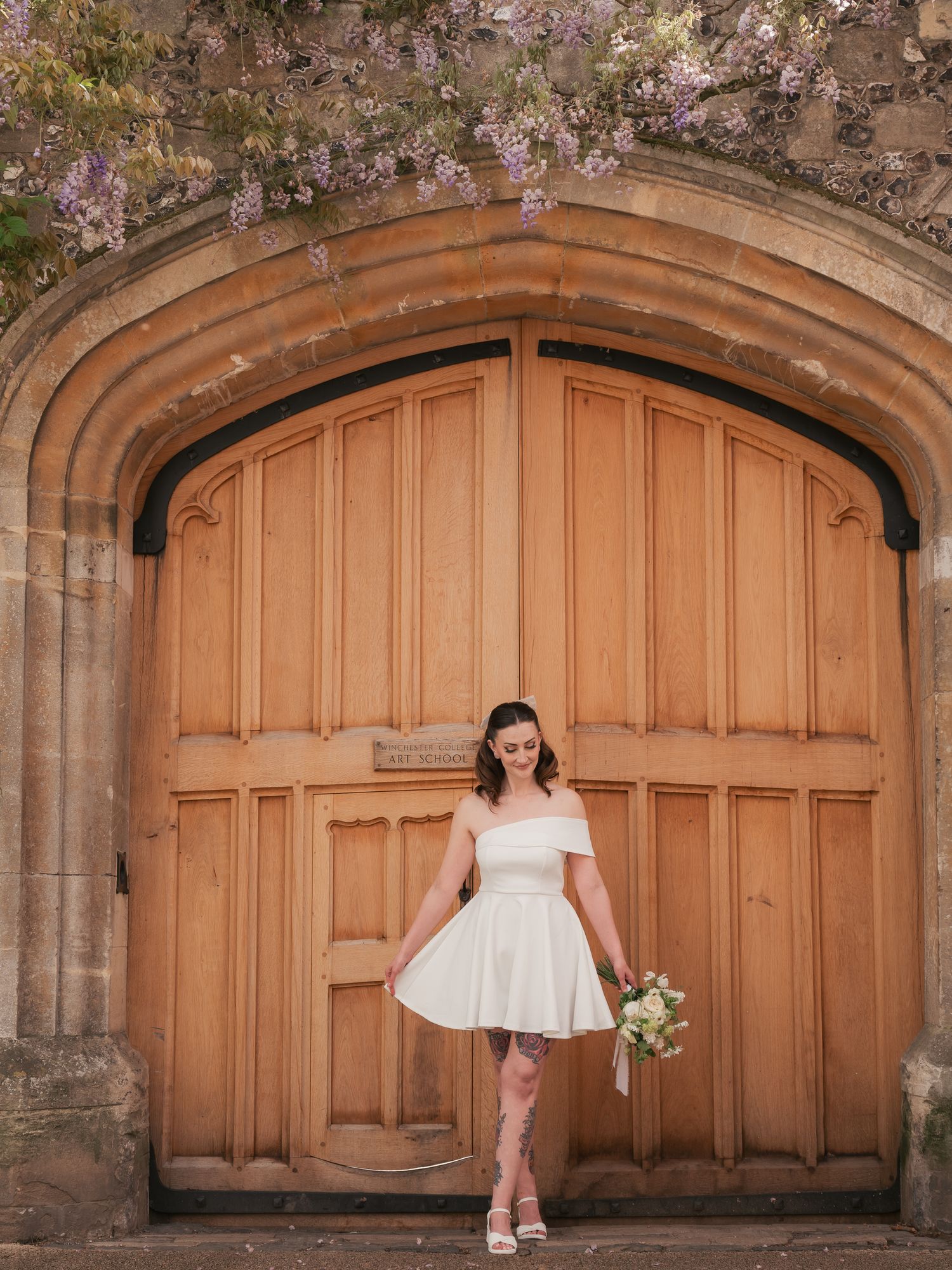 City bride in mini dress, stood outside large doors