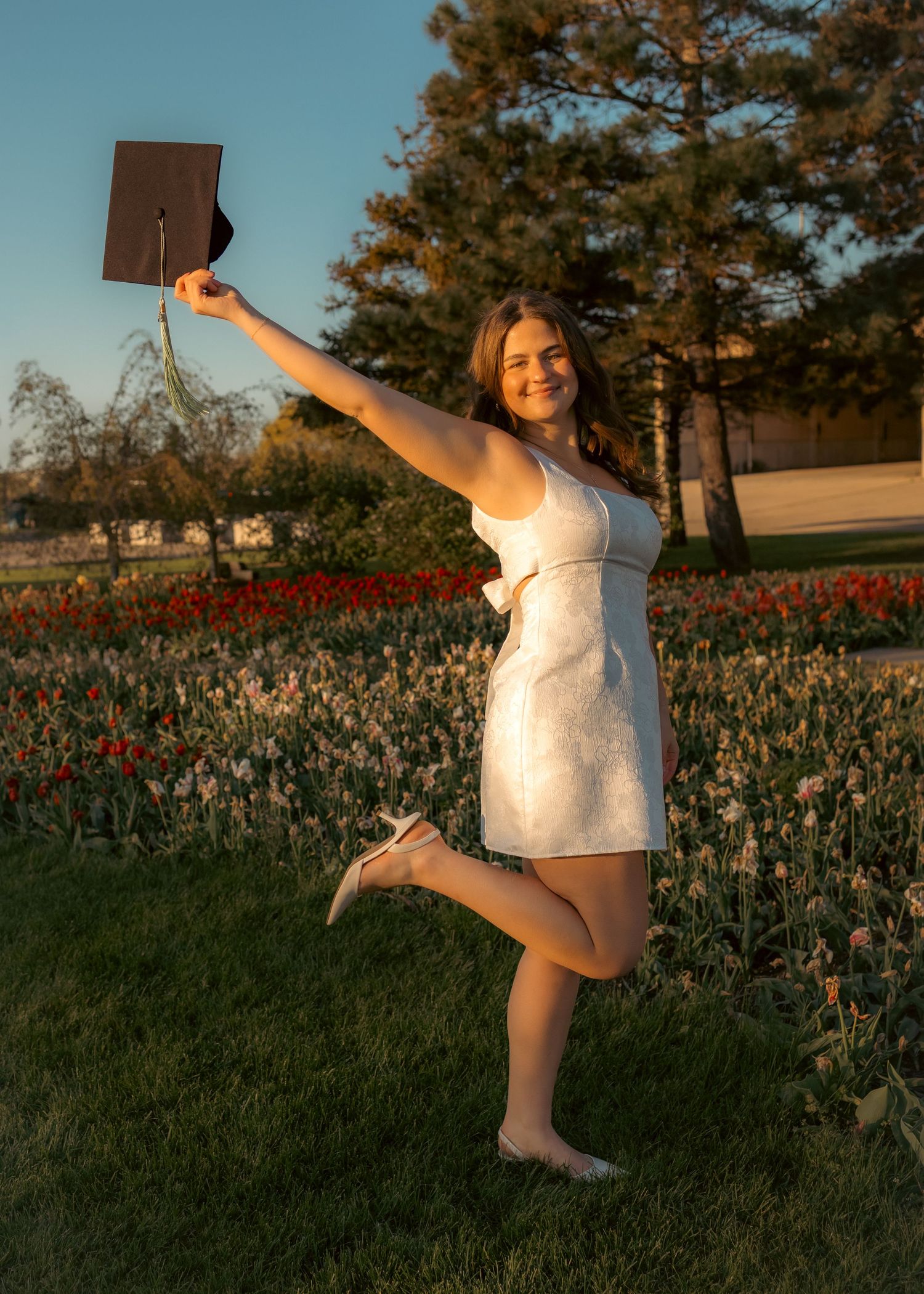 Playful outdoor portrait of a woman in a white dress holding a hat and jumping in a field
