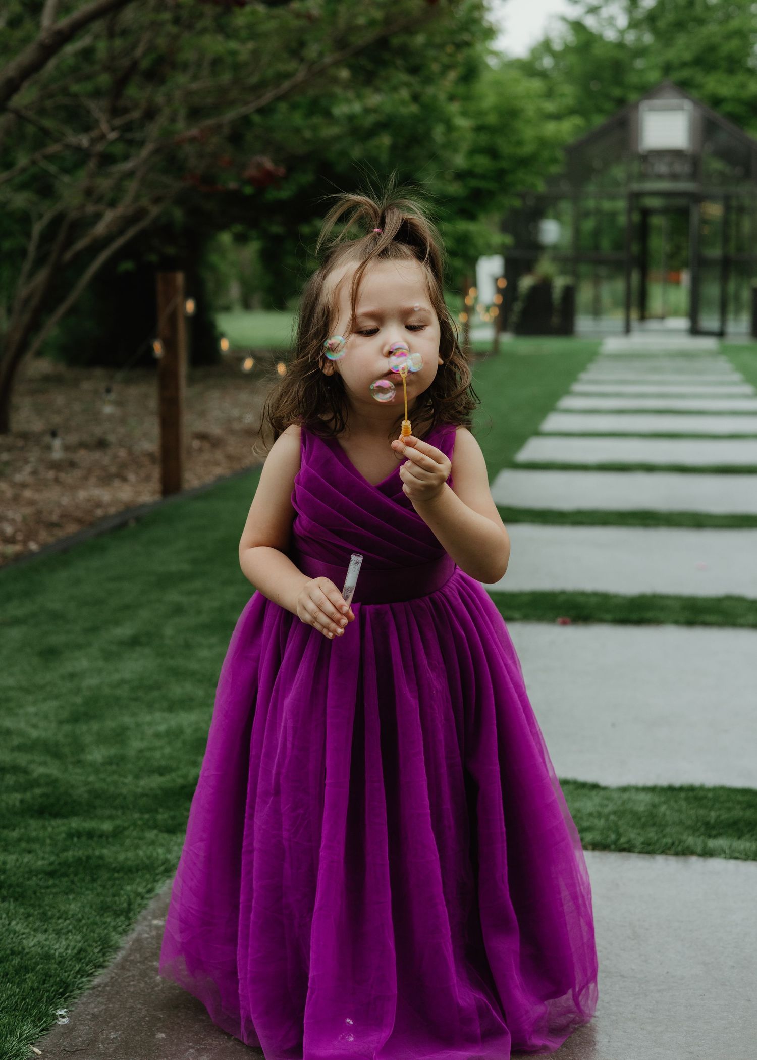 Young girl in a purple dress blowing bubbles outdoors