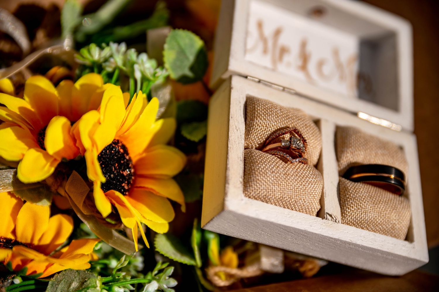 Wedding rings displayed in a rustic Mr. & Mrs. box beside vibrant sunflowers, perfect for a fall wedding.
