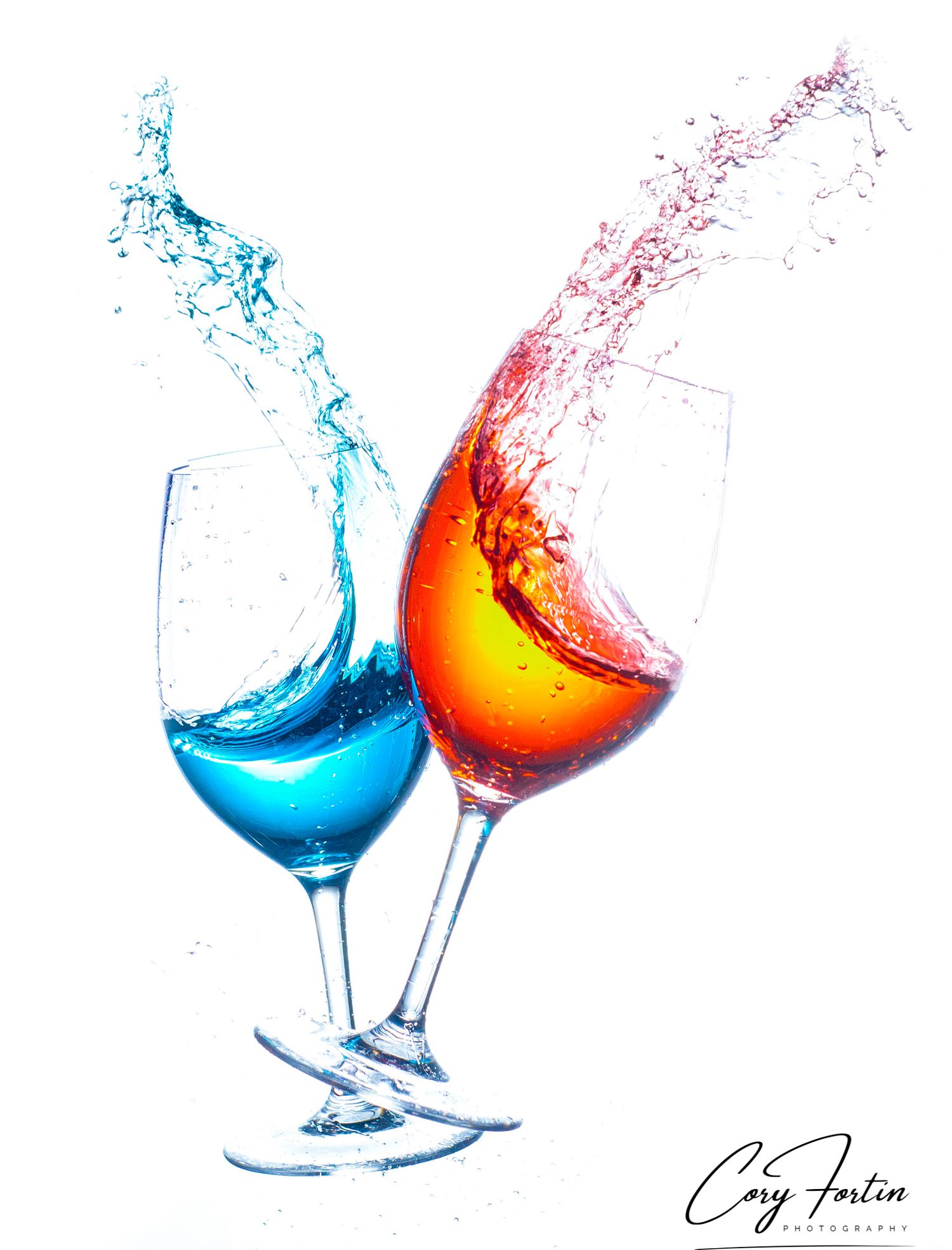 Two wine glasses with vibrant blue and orange liquid splashing dramatically against a white background.