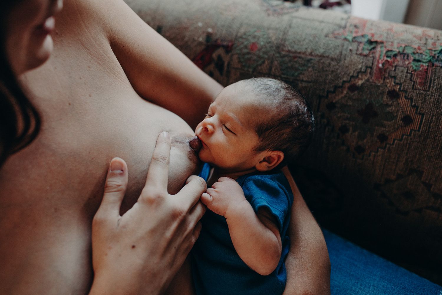 Newborn baby breastfeeding while being cradled by mother on a couch.