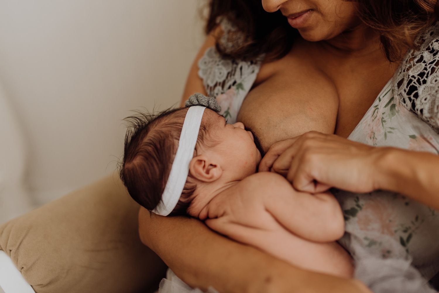 Mother tenderly cradling her sleeping newborn baby girl wearing a white headband during a lifestyle newborn session.