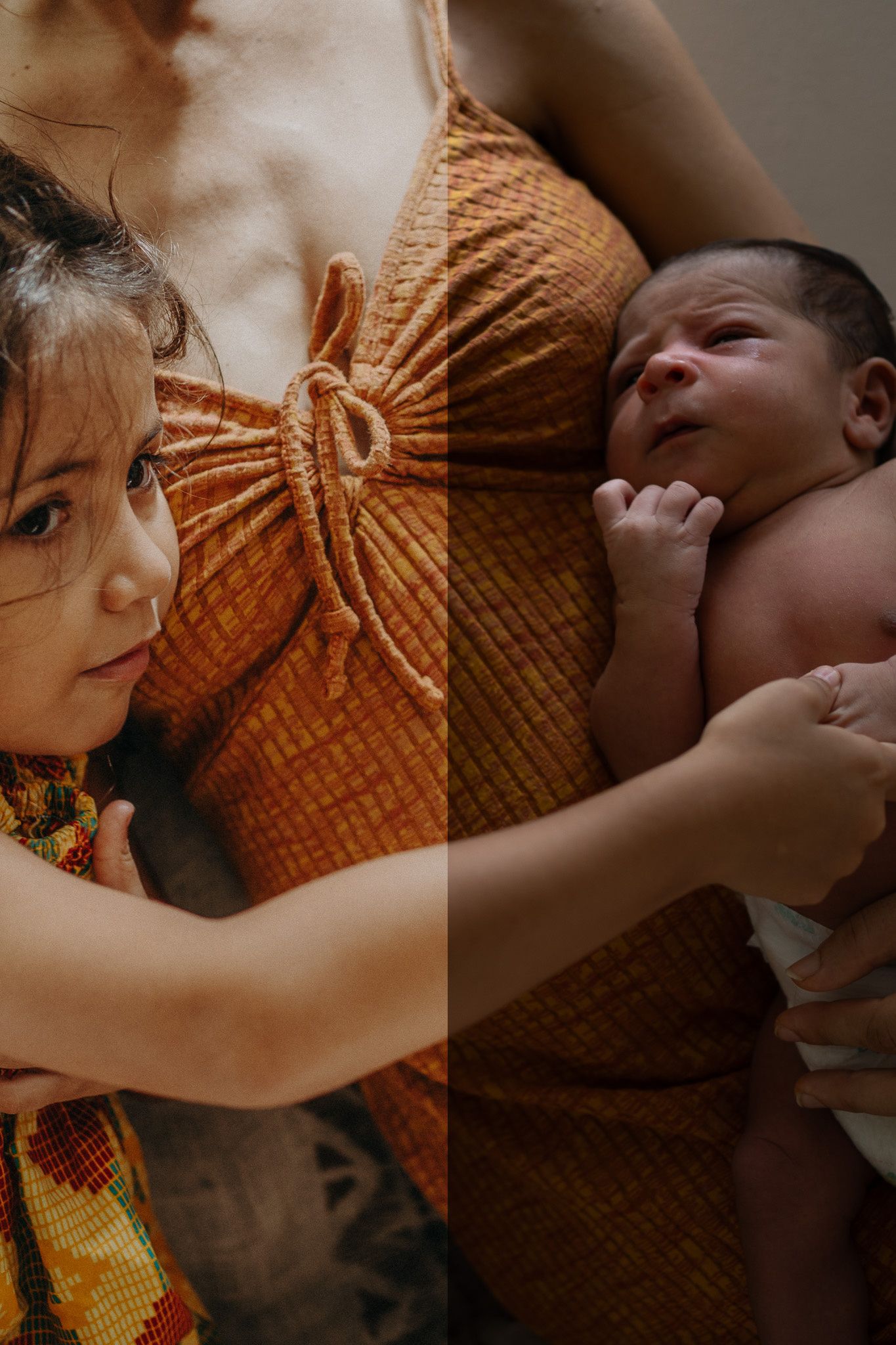 A young girl and a newborn baby cradled in the arms of a woman wearing an orange textured dress.