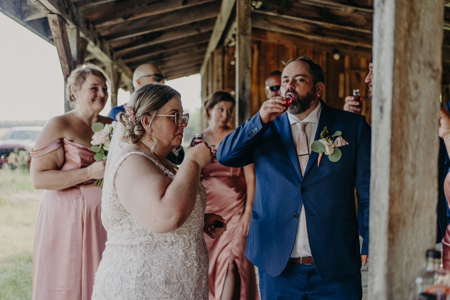 Bride and groom doing a shot together at their wedding reception with bridesmaids in pink dresses.