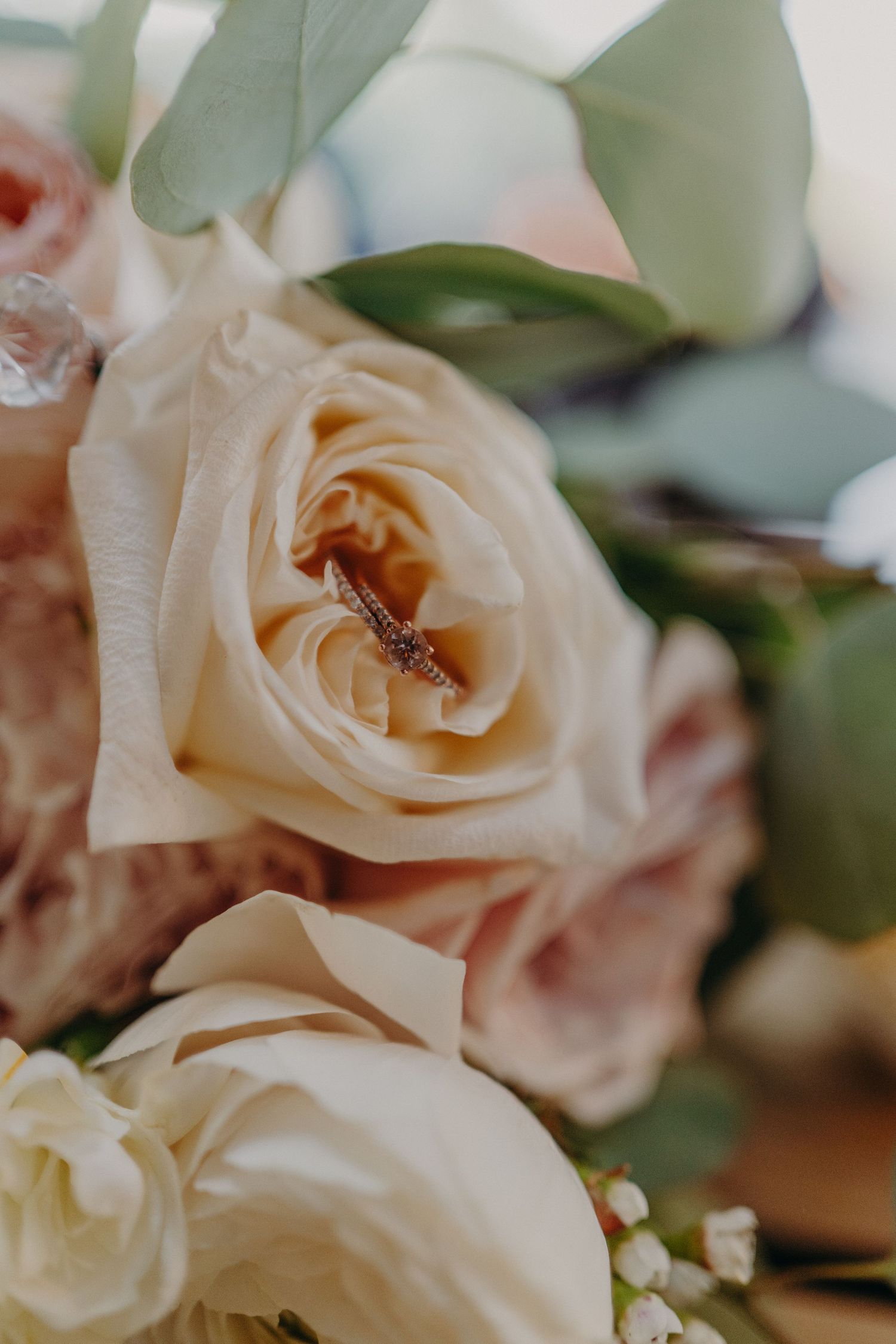 Close-up of a diamond wedding ring nestled inside a cream and blush rose bouquet.