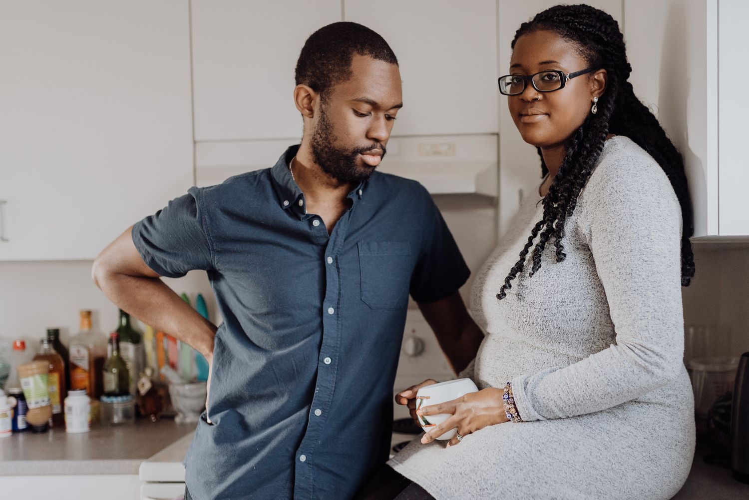 A Black couple shares a warm moment together in a modern kitchen, with the woman holding a cup.